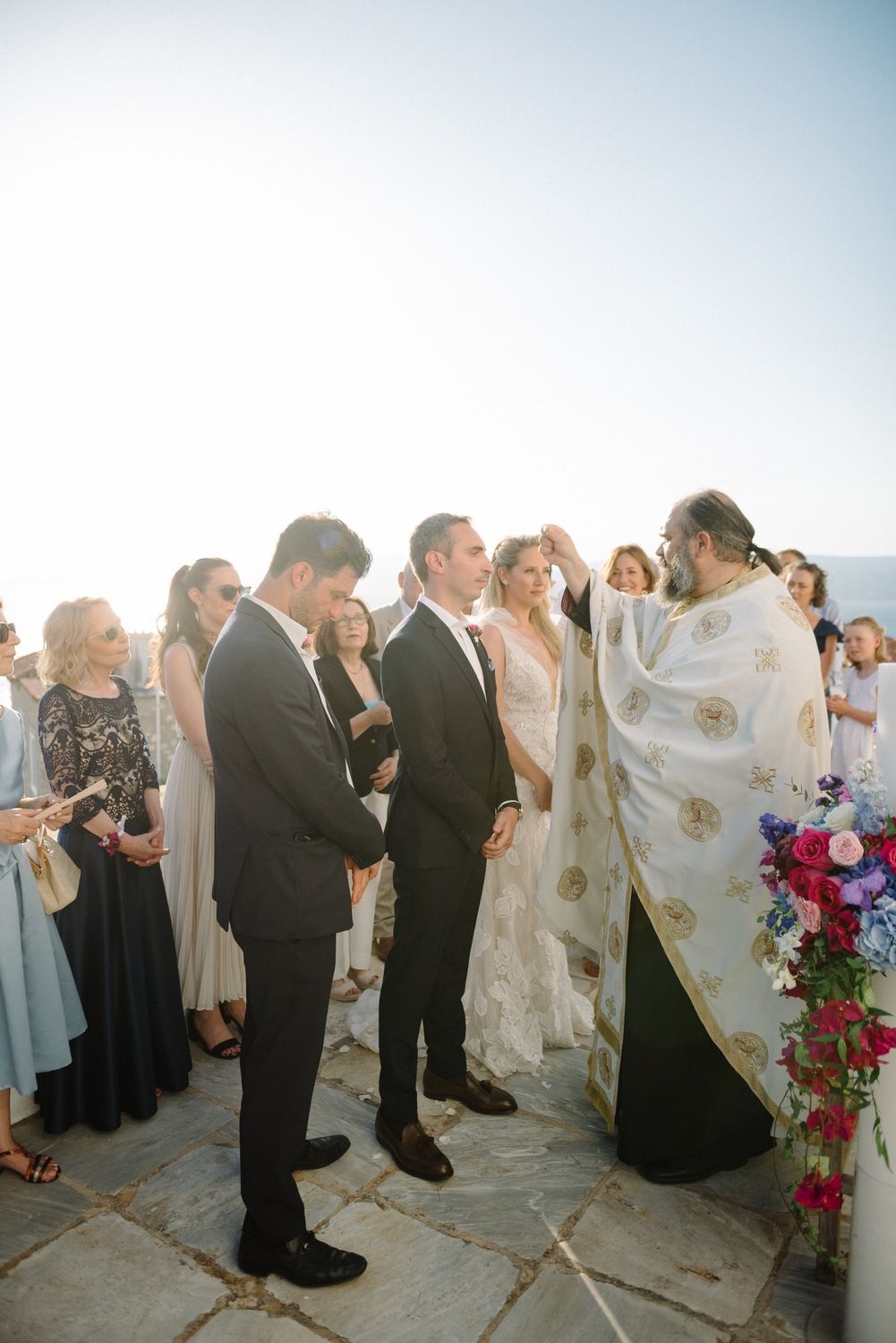 An intimate wedding ceremony moment captured against a bright sky with floral decorations.
