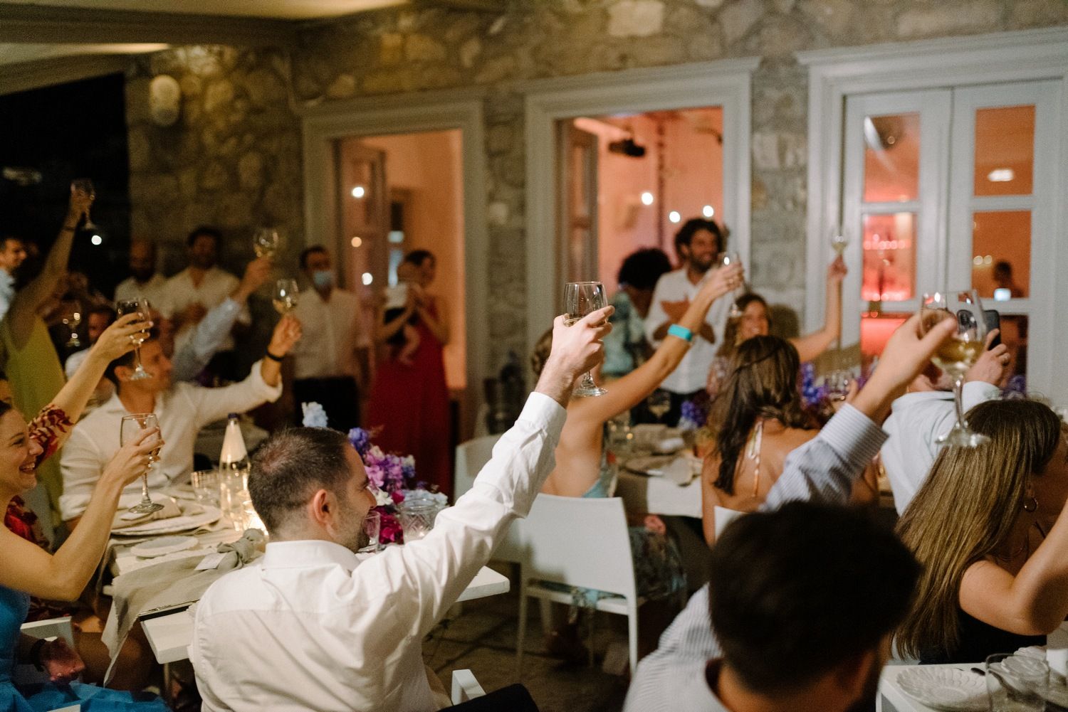 Energetic wedding reception scene with guests raising their hands in celebration.