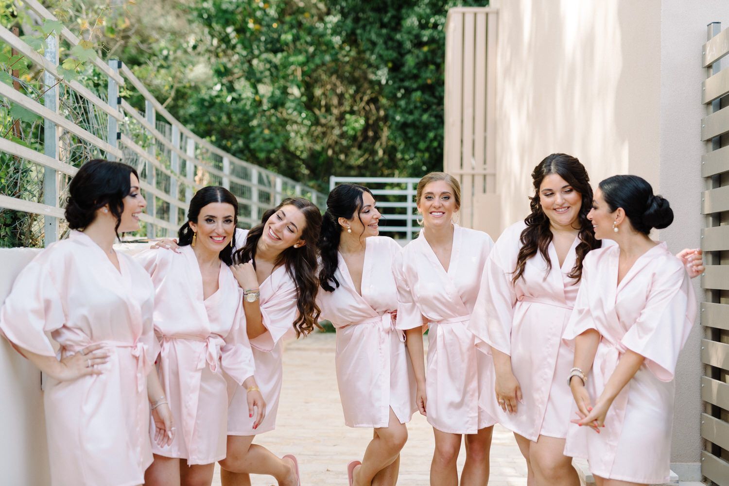 Group of bridesmaids in matching pink robes pose together outdoors.