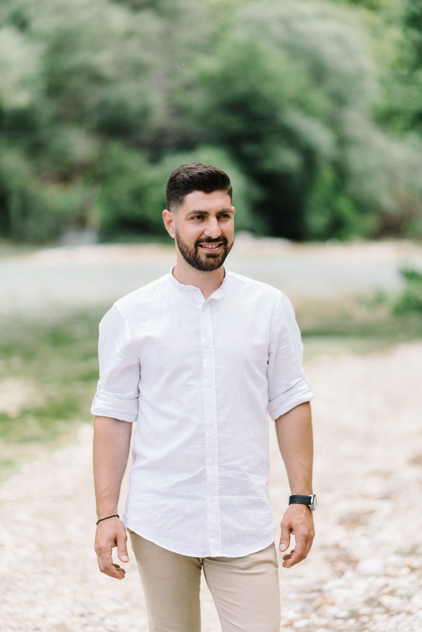 Person in crisp white shirt and khaki pants poses outdoors against a natural green background.