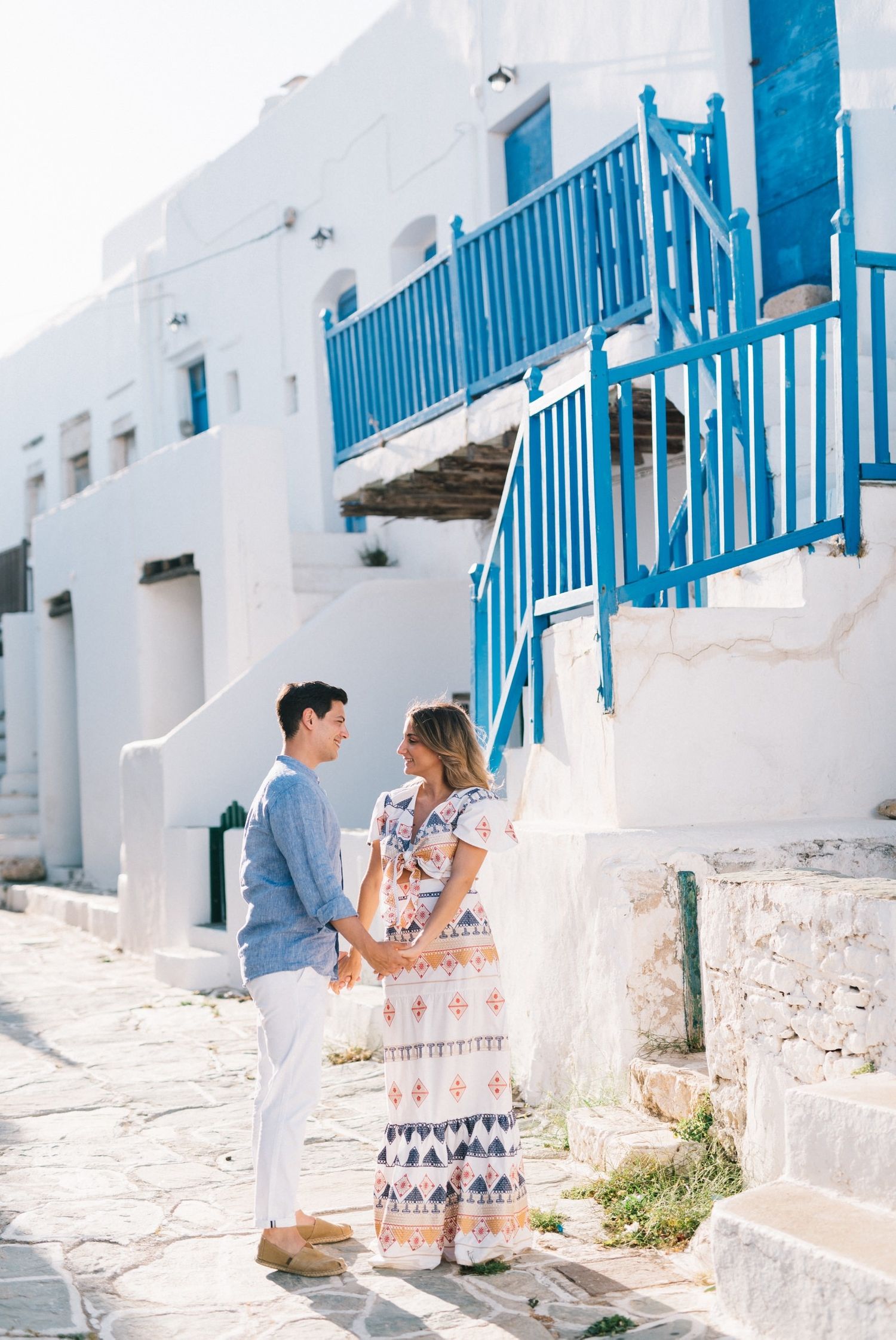 A couple shares a romantic moment on white stone steps with bright blue railings.
