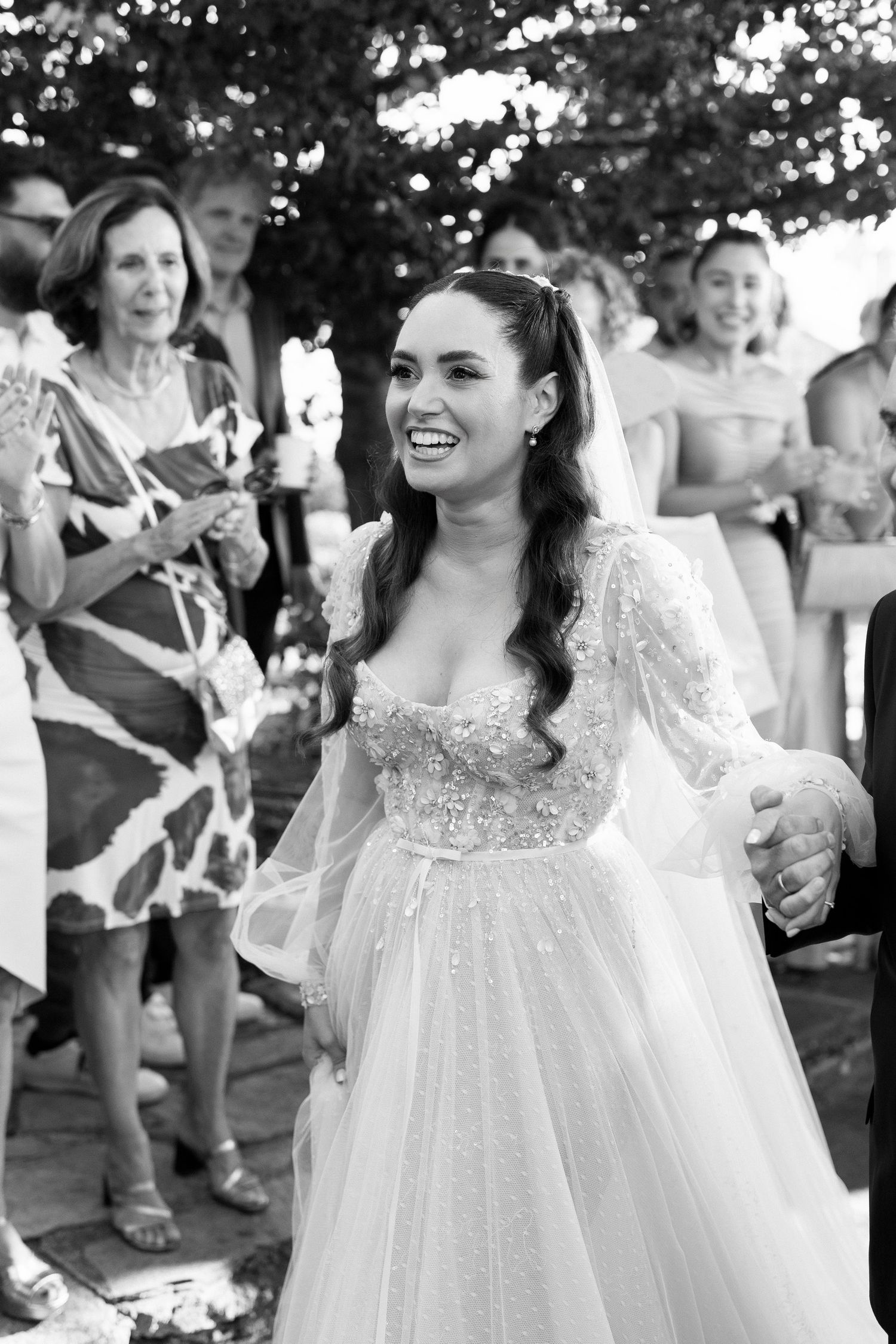 A radiant bride in a delicate lace and tulle wedding dress laughs joyfully while celebrating at an outdoor reception.