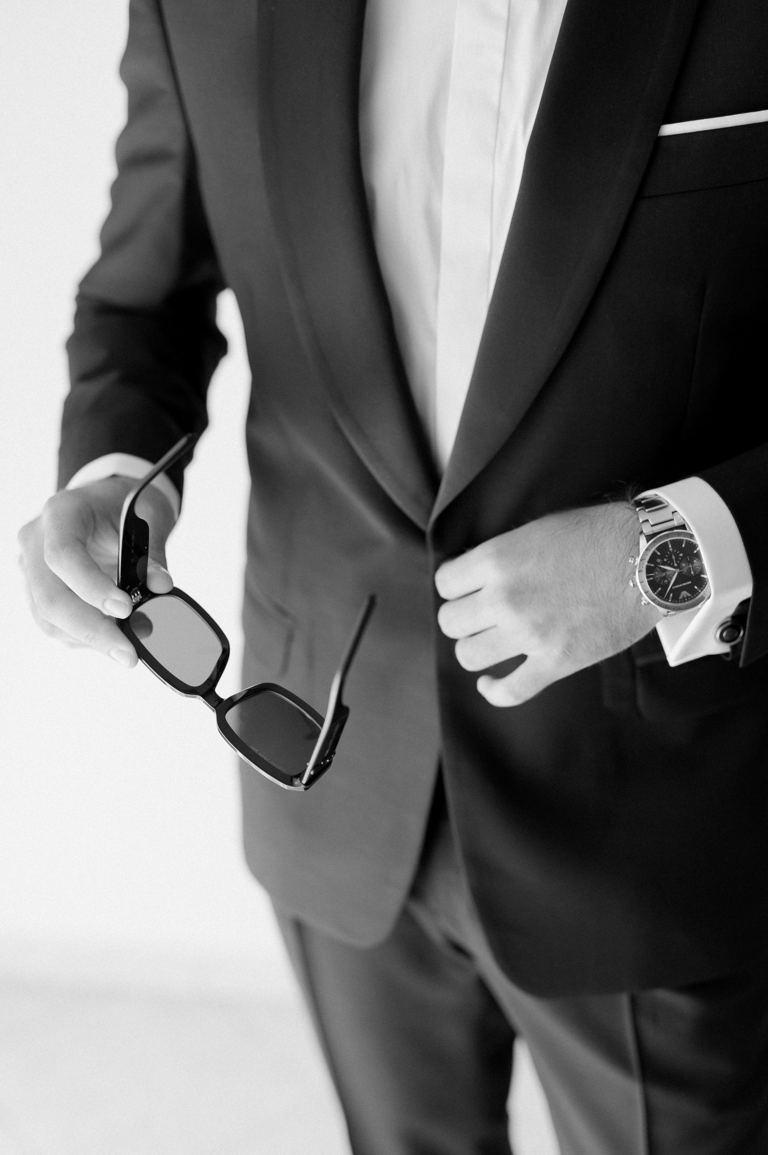 Close-up details of a formal black suit jacket with white shirt and silver watch showing professional business attire.