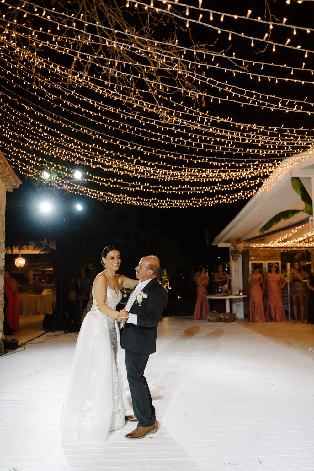 A romantic dance under a canopy of twinkling fairy lights at an evening wedding reception.