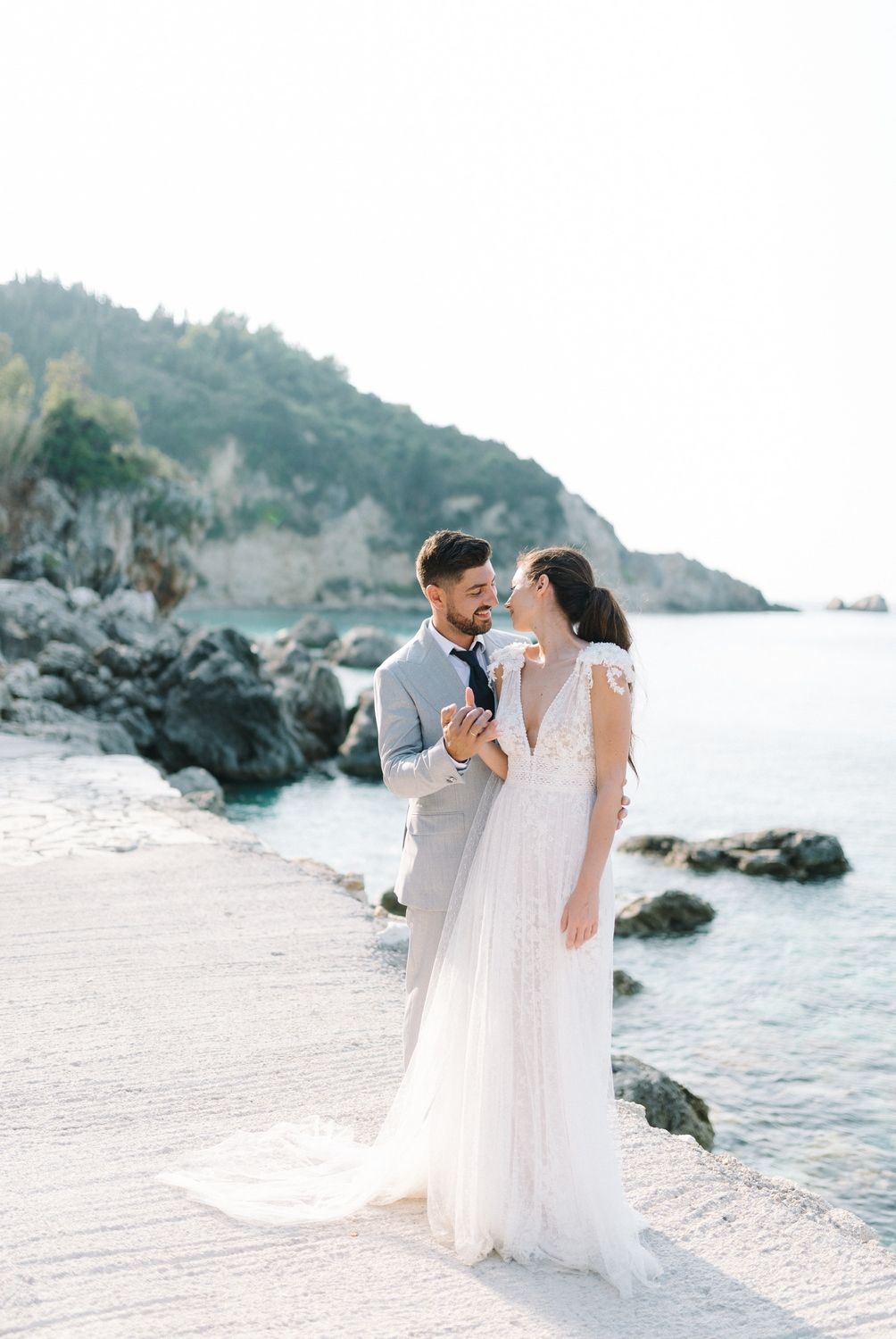 Romantic coastal wedding photo with rocky beach and ocean backdrop.