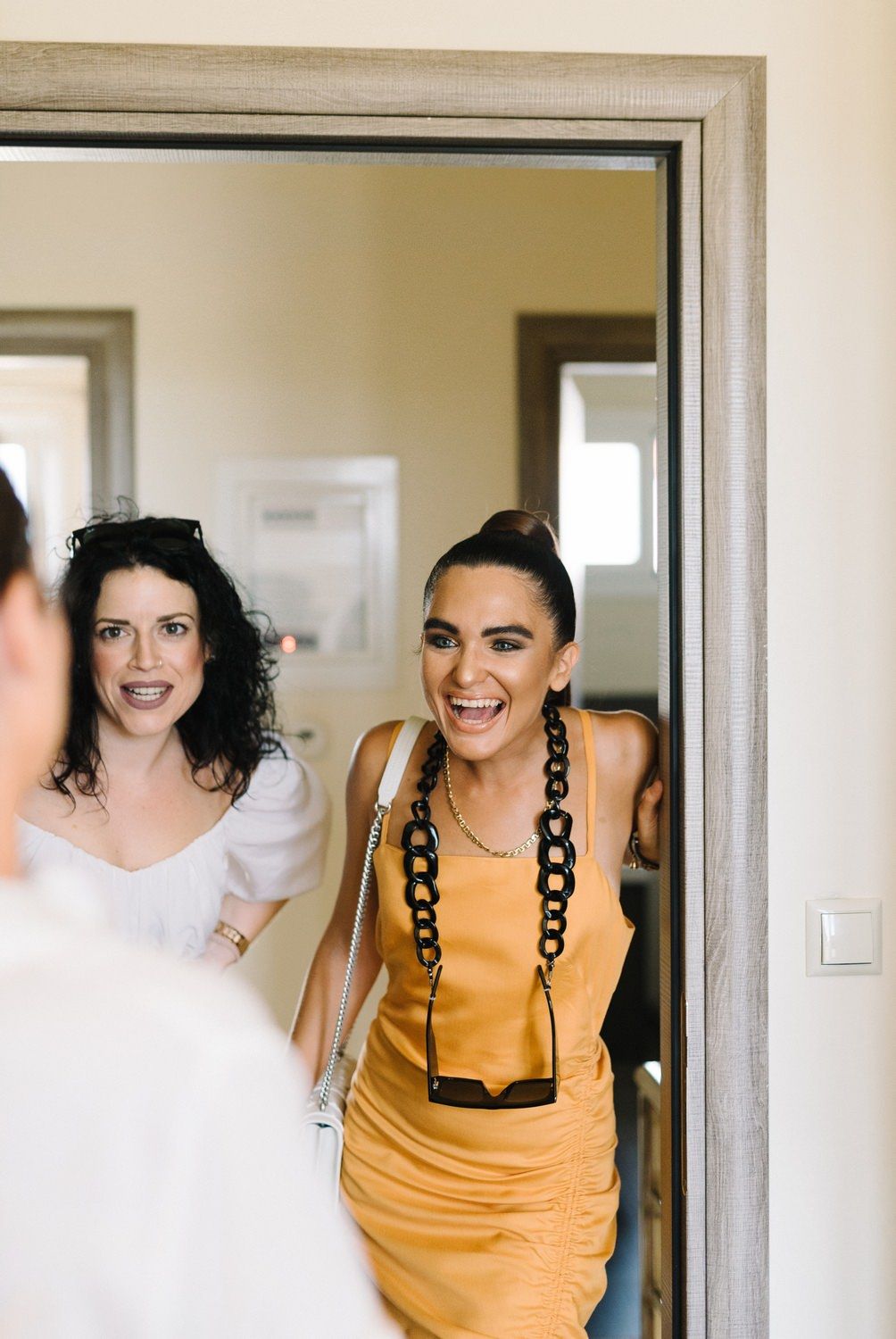 Wedding party members sharing joyful moment together in bright room with mirror.