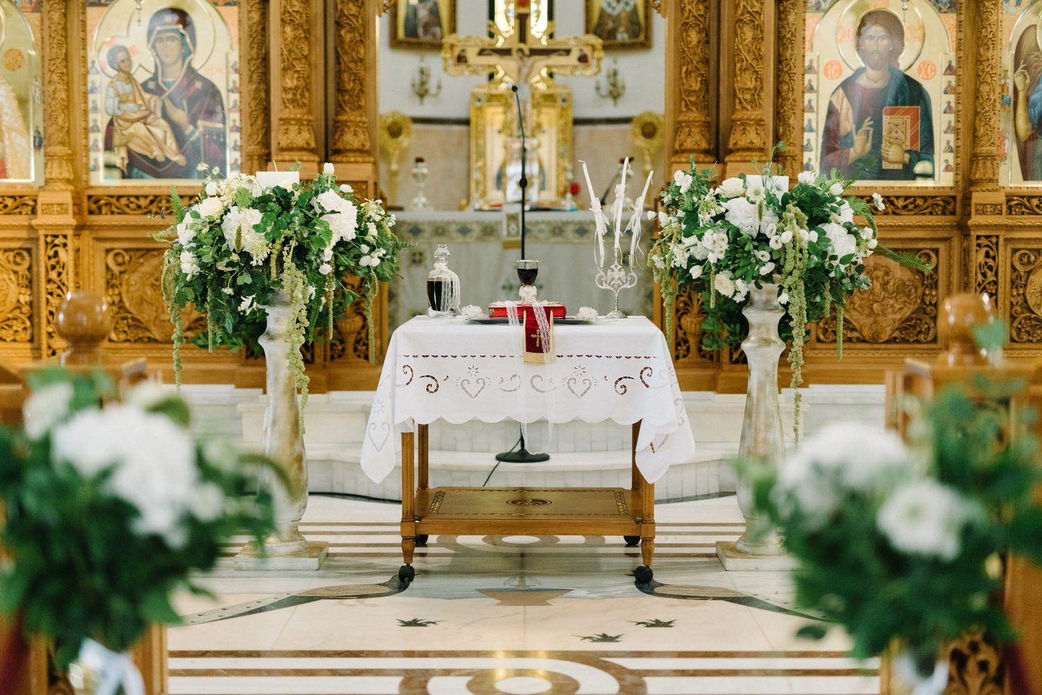 Ornate church altar decorated with white floral arrangements, candles, and golden icons for a wedding ceremony.