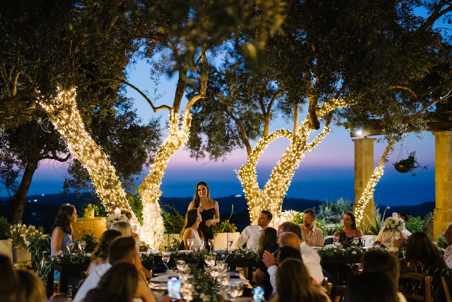 Outdoor wedding reception at dusk with illuminated trees creating a magical atmosphere.