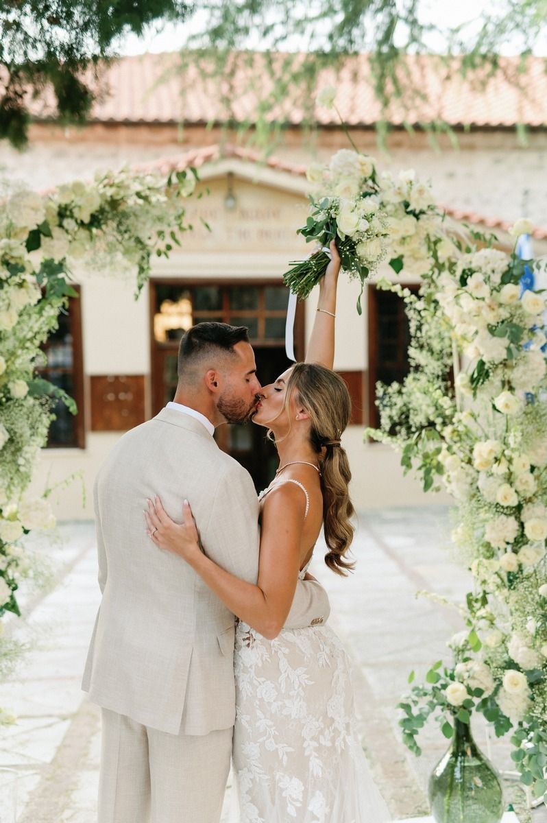 Intimate wedding portrait under arch adorned with white flowers and greenery.