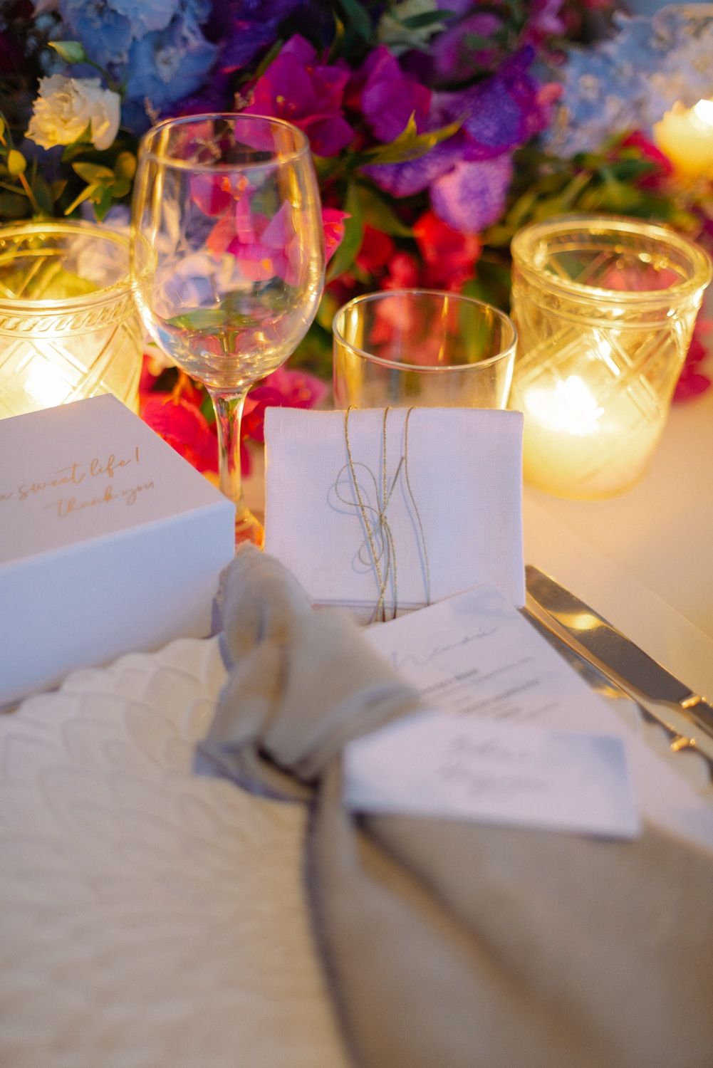 Romantic table setting with candlelight, wine glasses and white place cards among colorful flowers.