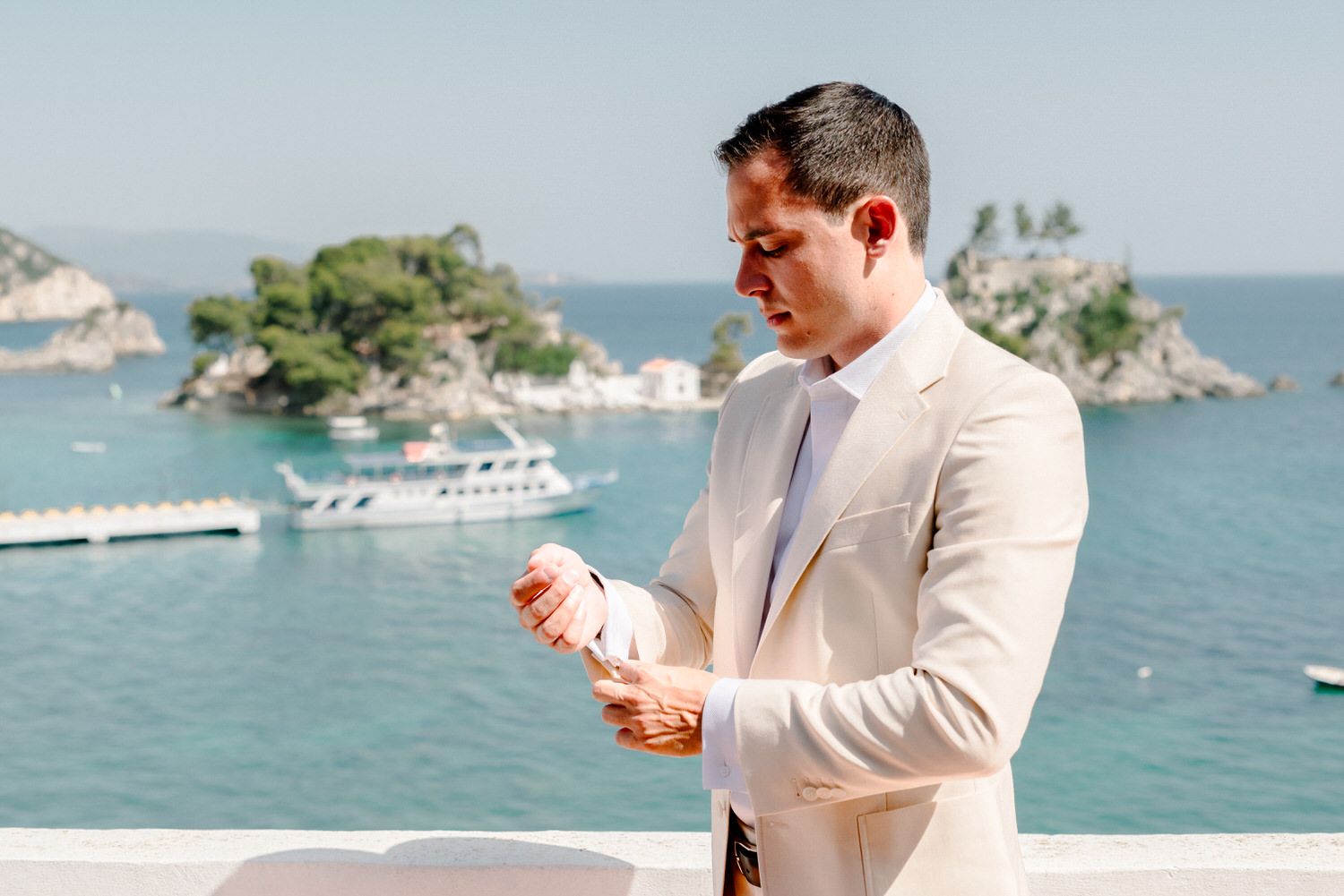 Person in a light beige suit checks something on a balcony with ocean and islands in background.