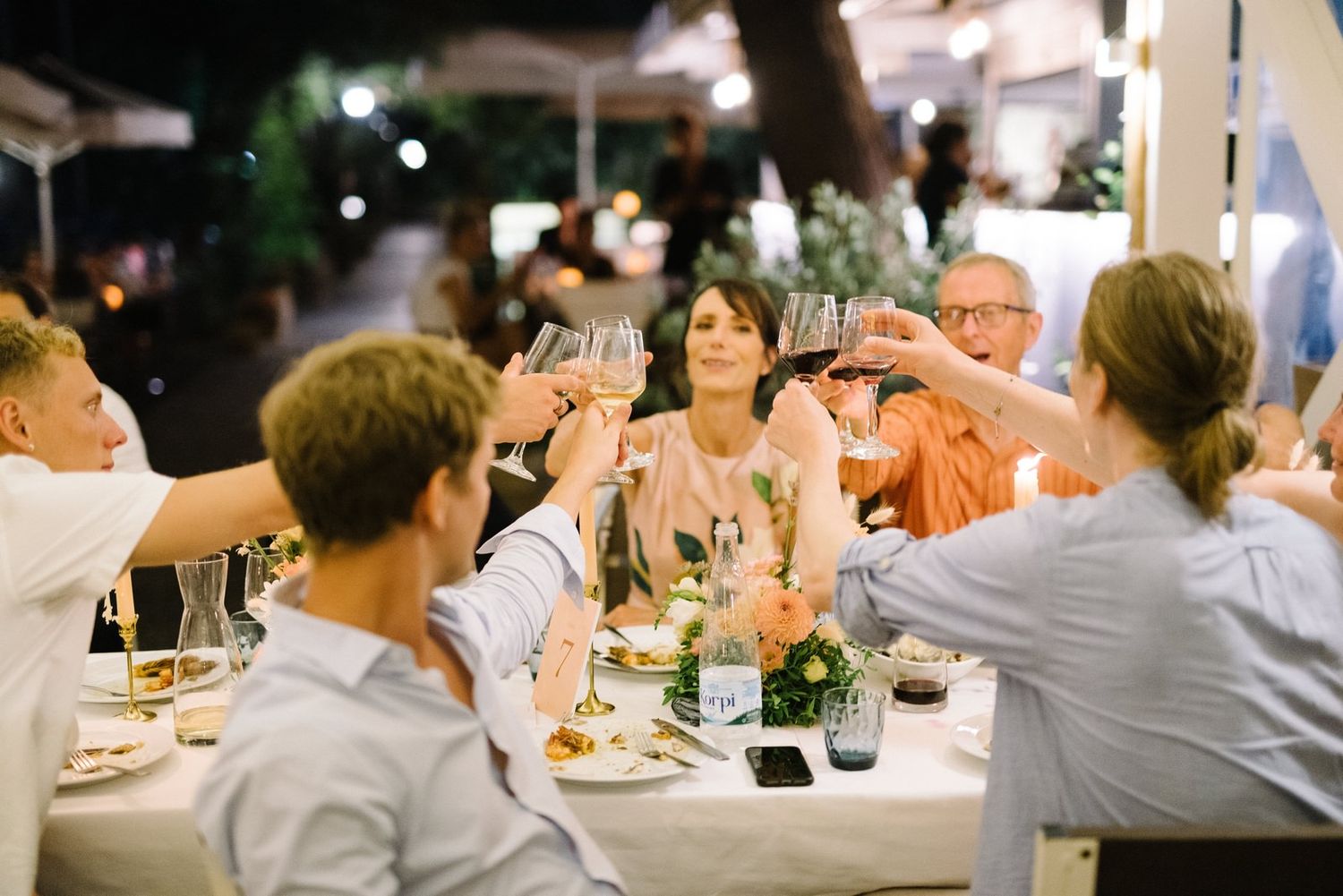 Wedding guests raise glasses for a toast during outdoor reception dinner.