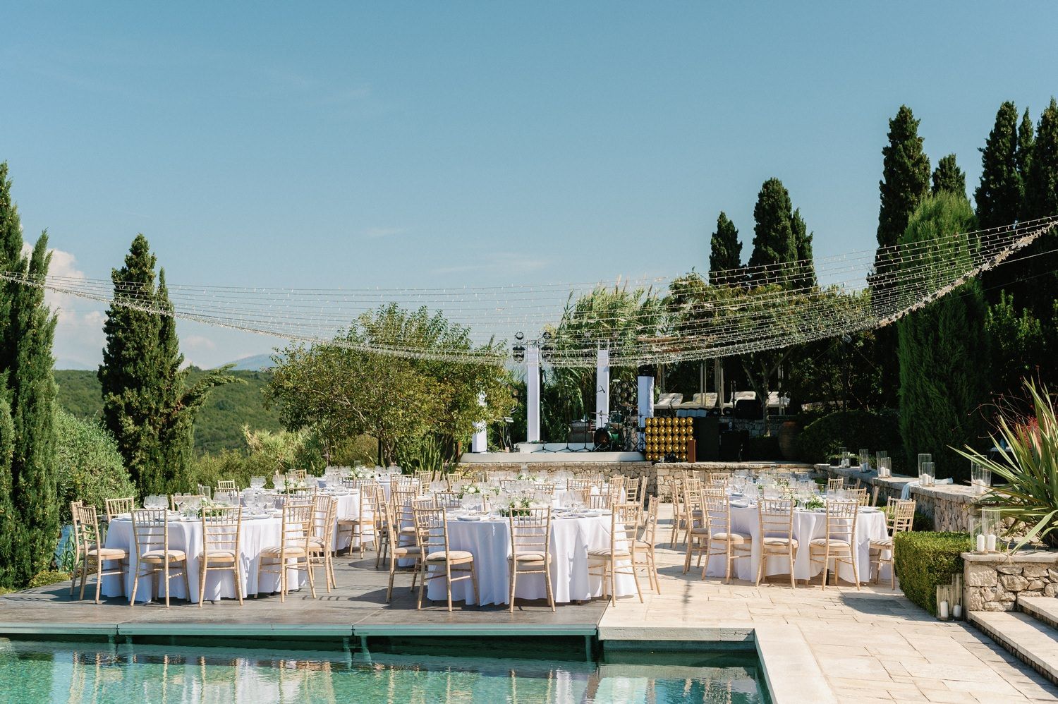 Elegant outdoor wedding venue with pool, string lights and white table settings.