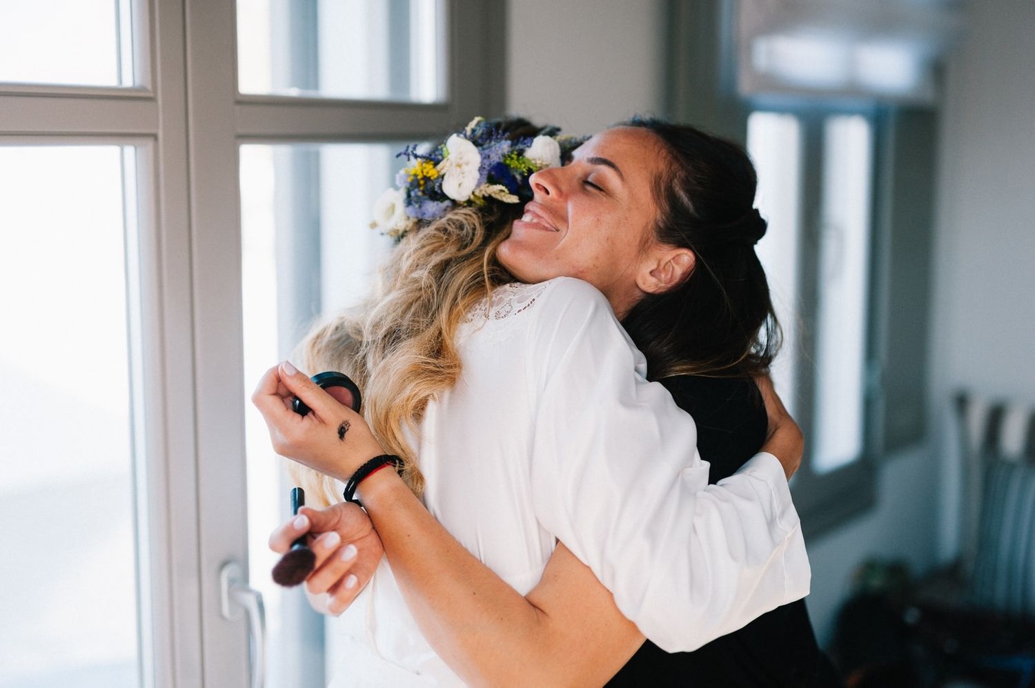 Two women embracing joyfully while wearing white and decorated with floral hair accessories.