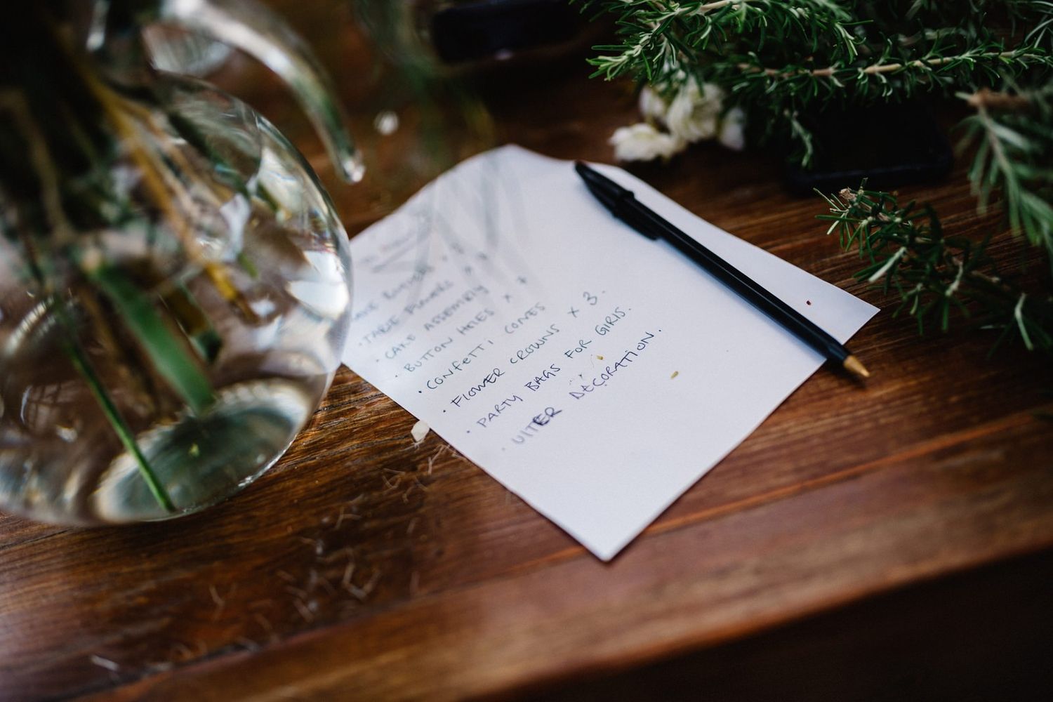 A handwritten note on white paper placed on a dark wooden surface with greenery in the background.