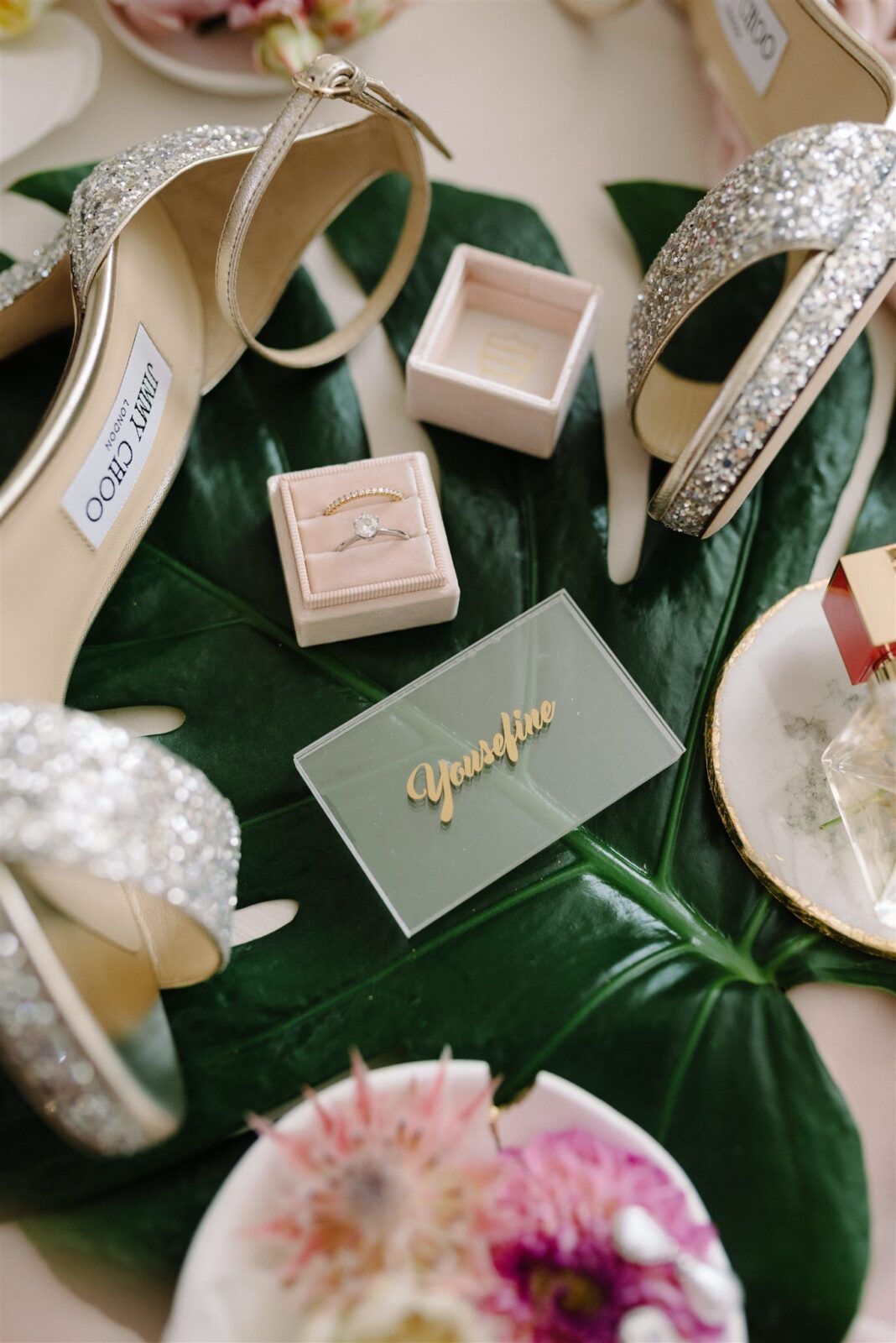 Wedding favor boxes and decorative elements arranged on dark green monstera leaves with pink floral accents.