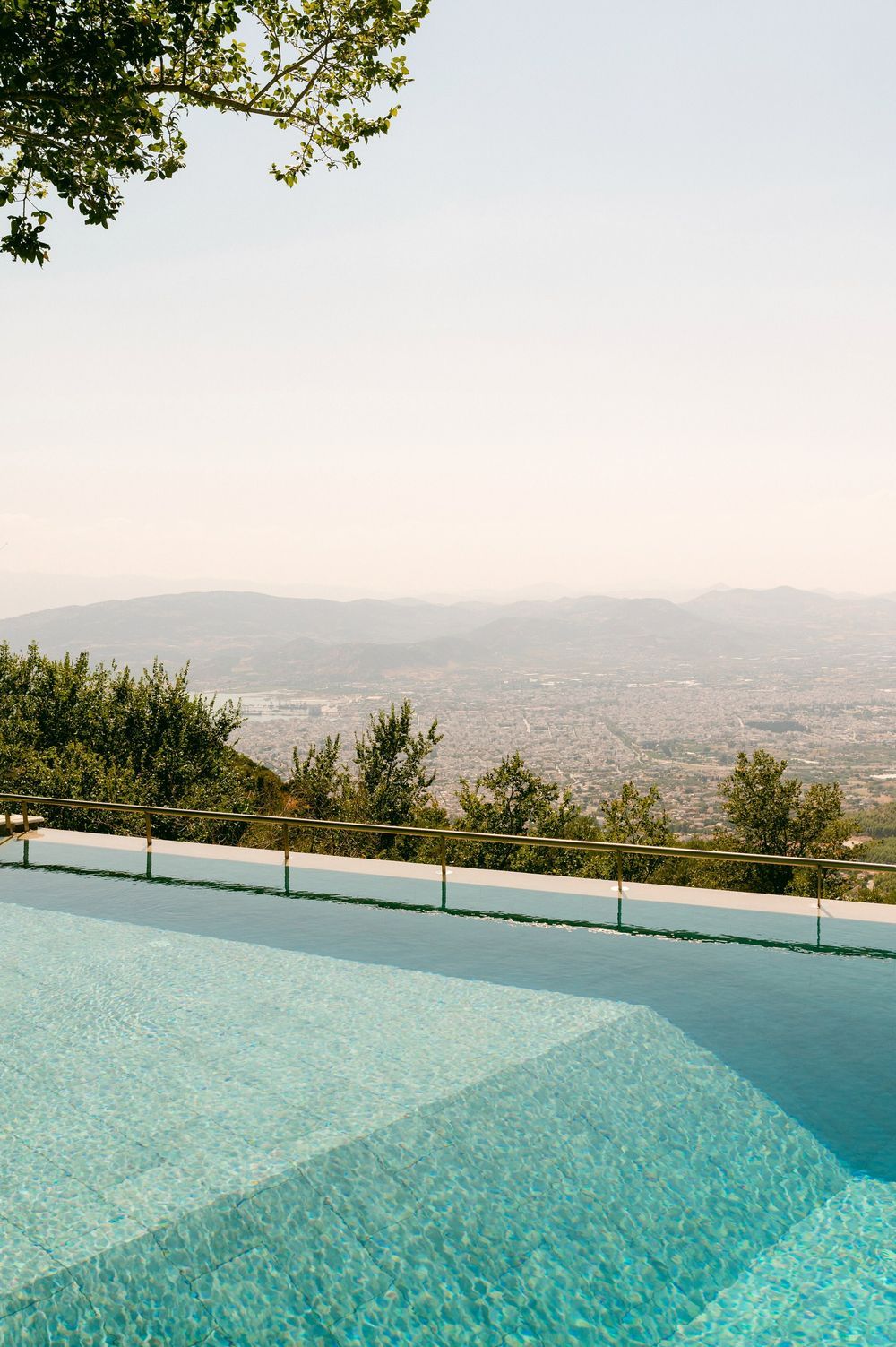 Panoramic view of an infinity pool overlooking a scenic mountain valley with turquoise water reflecting the sky.