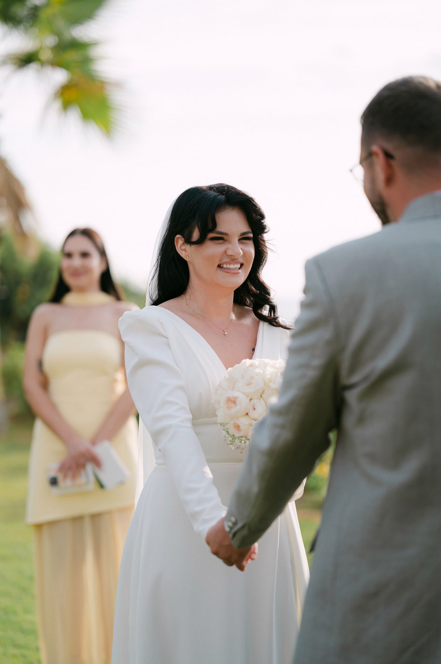 A wedding ceremony outdoors with the wedding party in yellow bridesmaid dresses and gray suits.