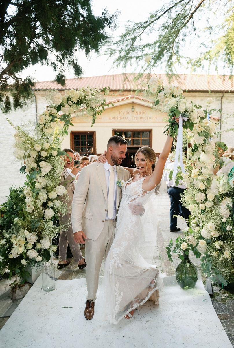 Newlyweds celebrate under beautiful white floral arch at outdoor ceremony.
