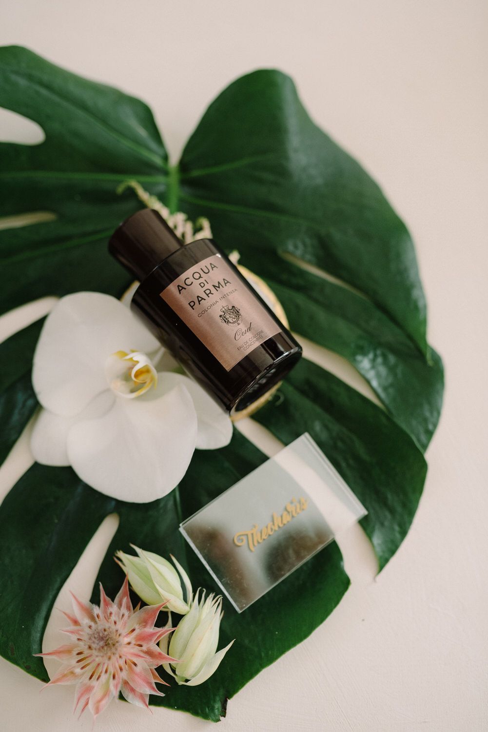 Perfume bottle and white orchid arranged on large monstera leaf for wedding detail shot.