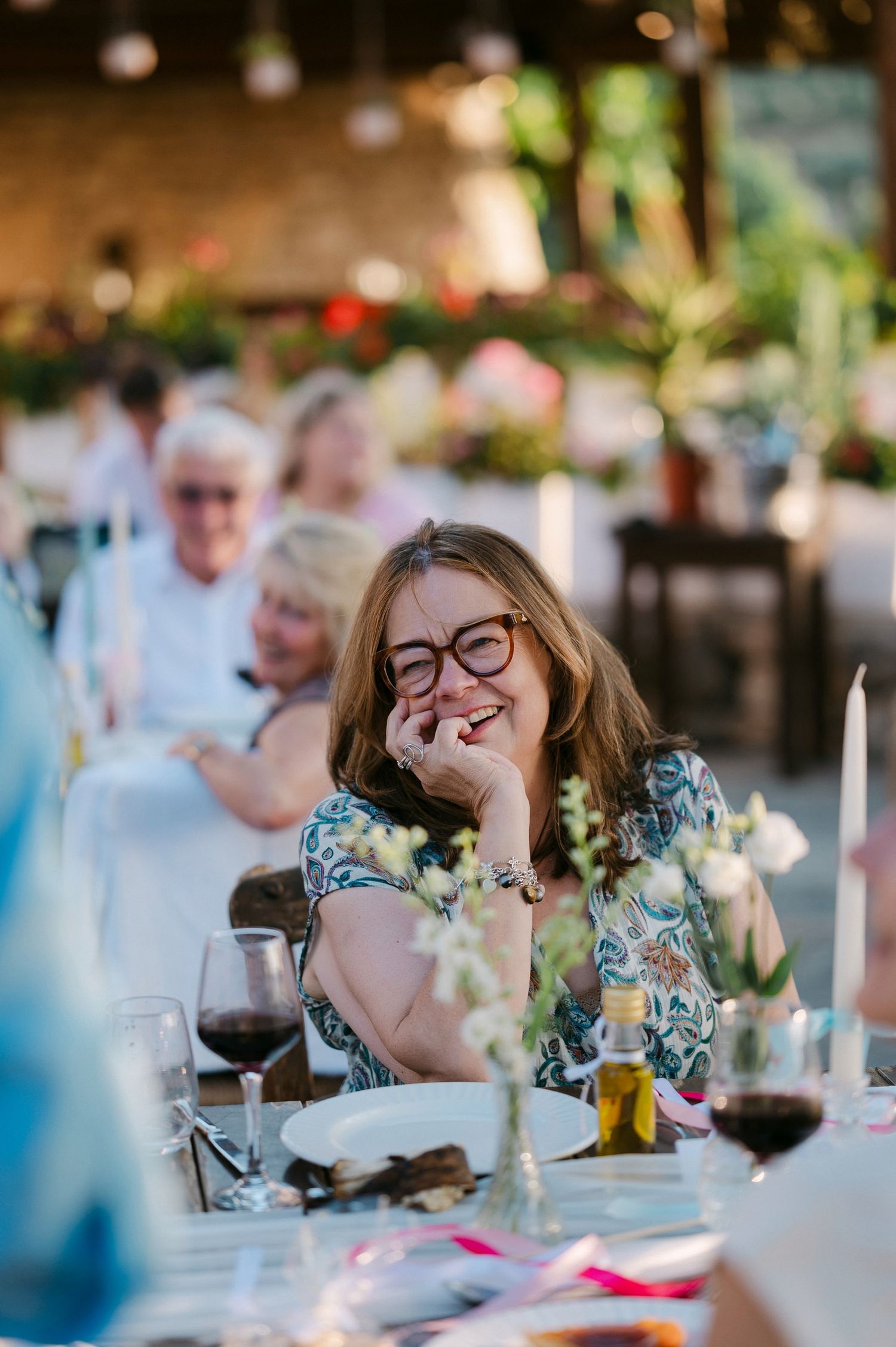 Wedding guest laughing joyfully at reception dinner table with wine glass in hand.