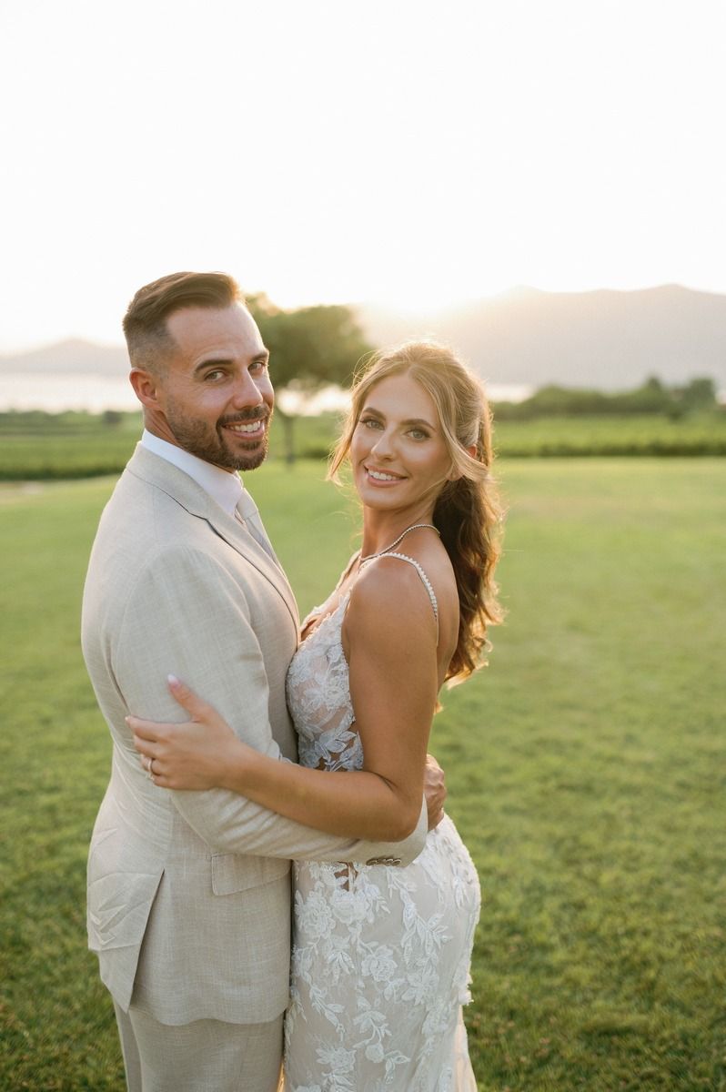 A happy couple embraces on a sunlit lawn during golden hour in wedding attire.