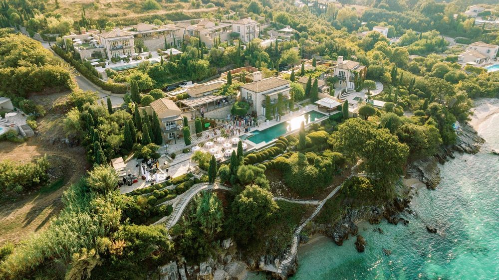 Aerial view of a luxury coastal resort with turquoise waters, white buildings, and lush tropical landscaping.