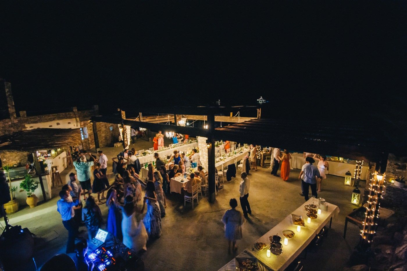 Outdoor evening wedding reception venue overlooking the sea with string lights creating ambiance.