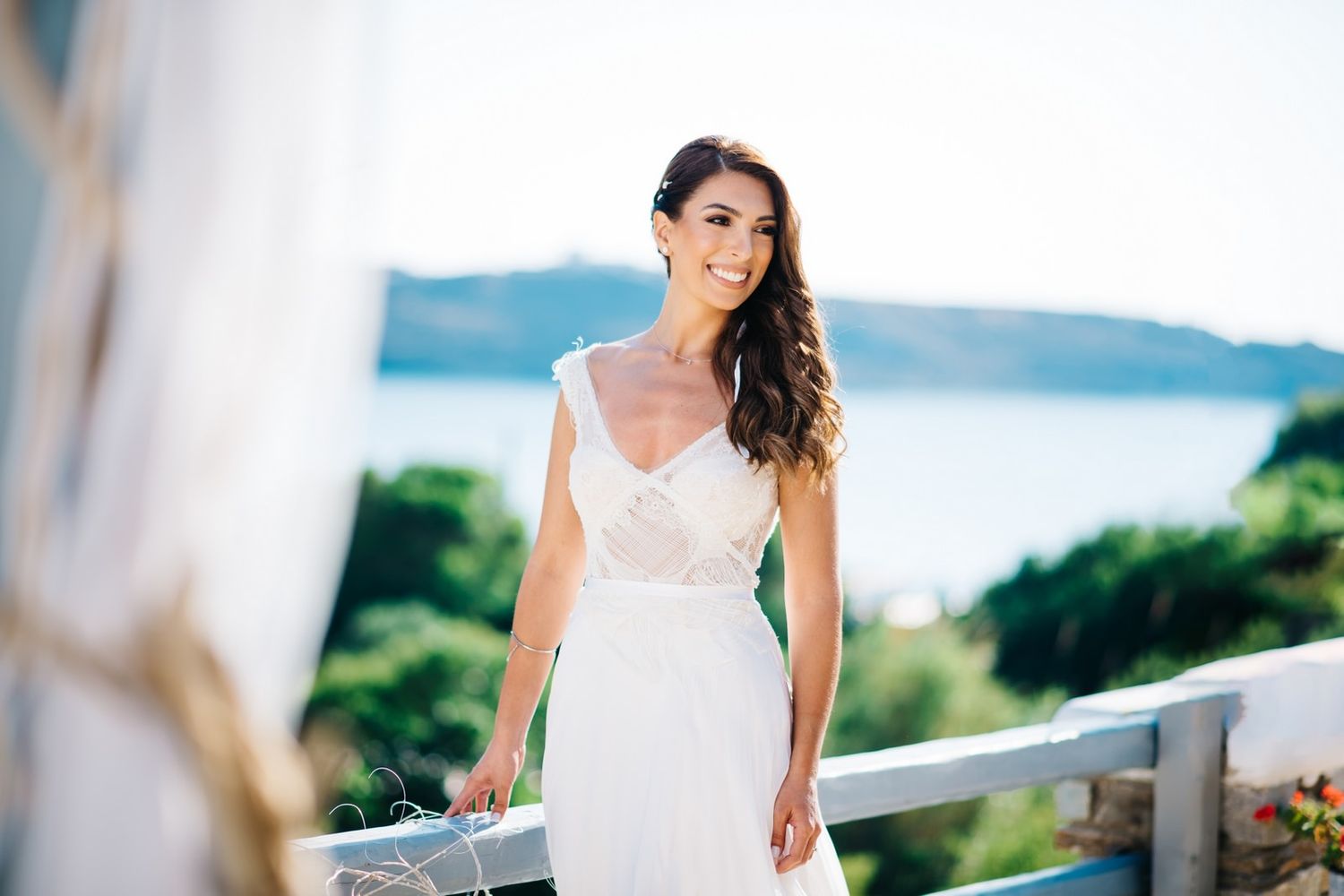 An elegant white wedding gown photographed against a bright coastal backdrop with palm trees.