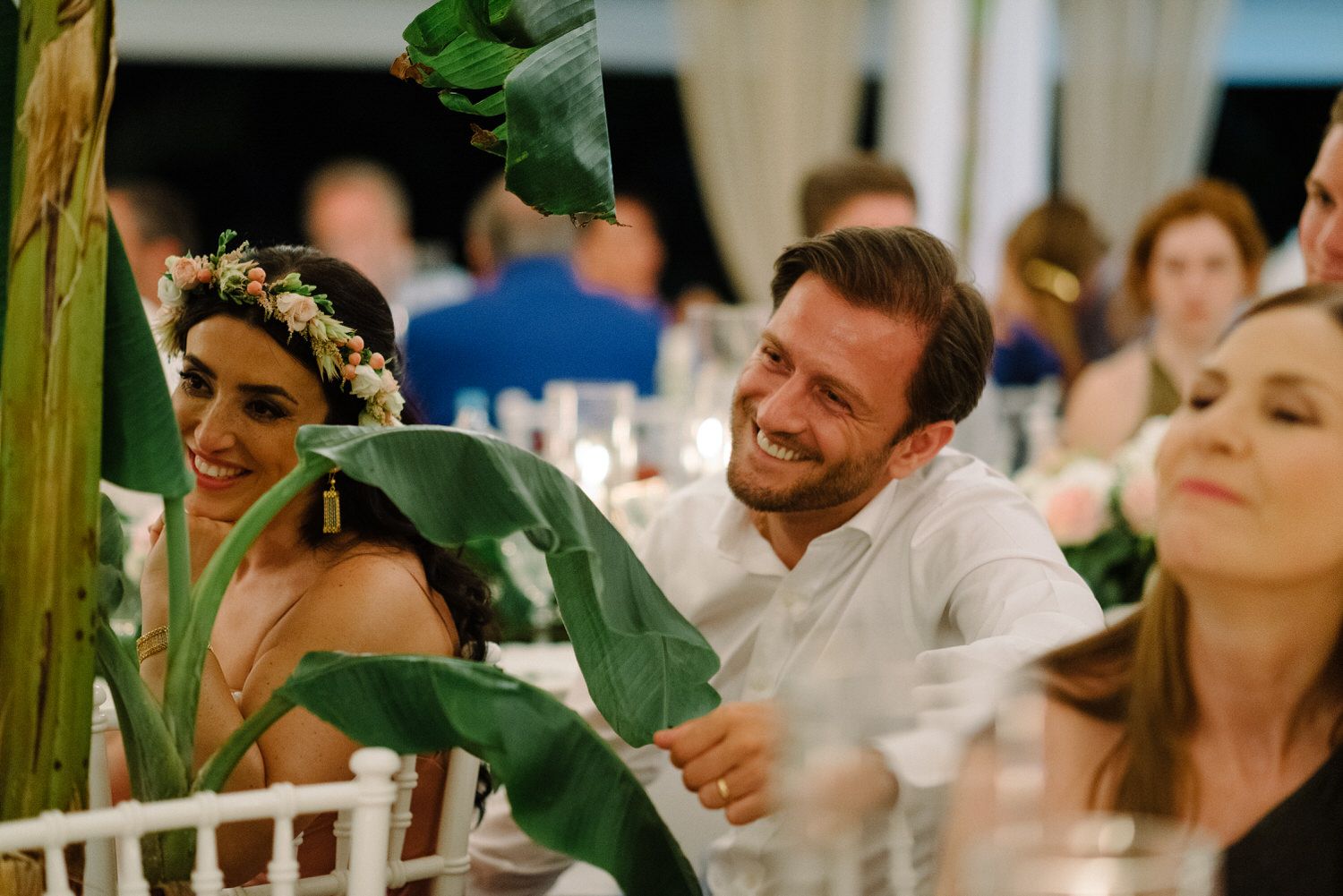 Wedding guests enjoying a candlelit reception under tropical foliage and string lights.