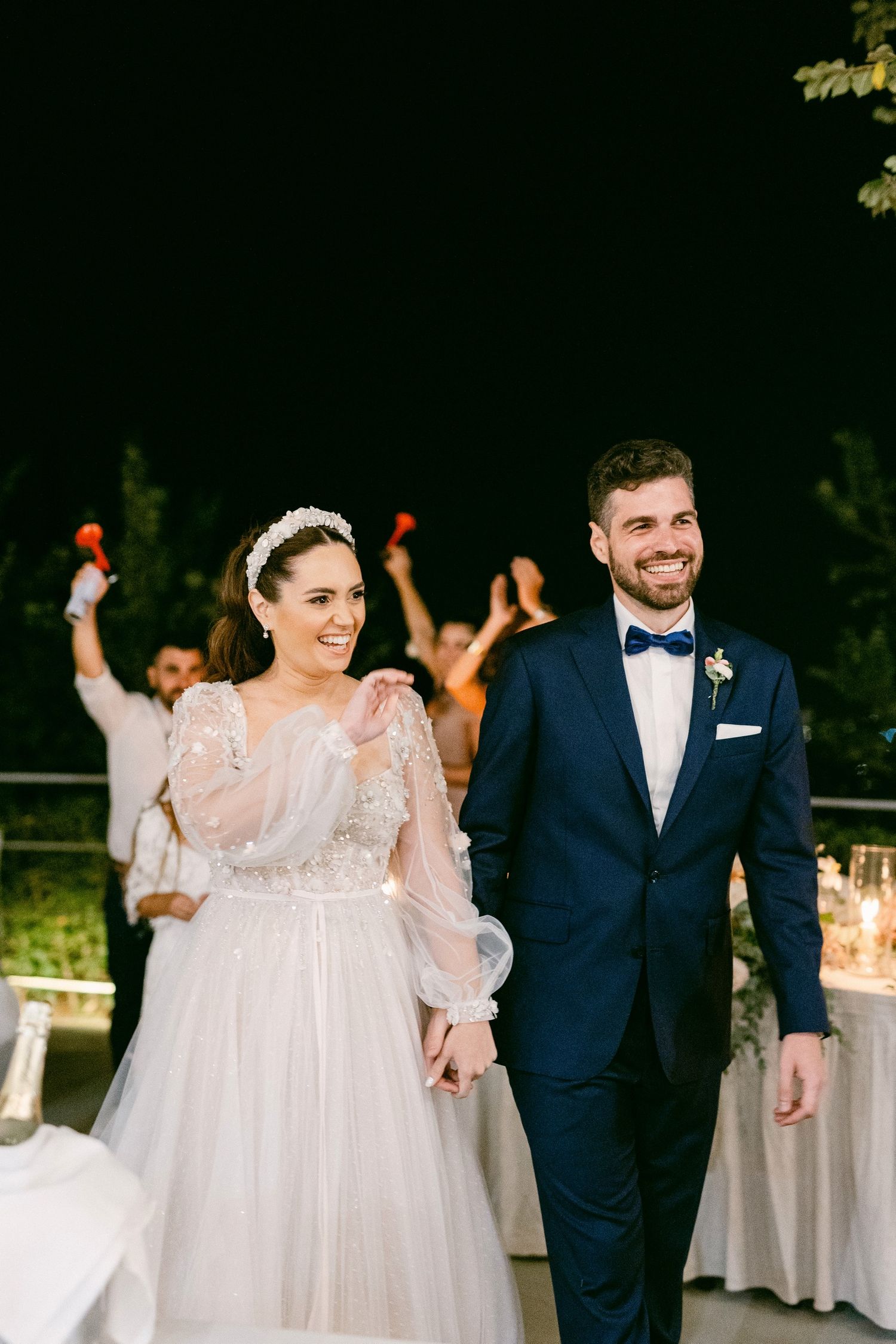 Couple at their evening wedding celebration with the bride in flowing white dress and groom in navy suit with bowtie.