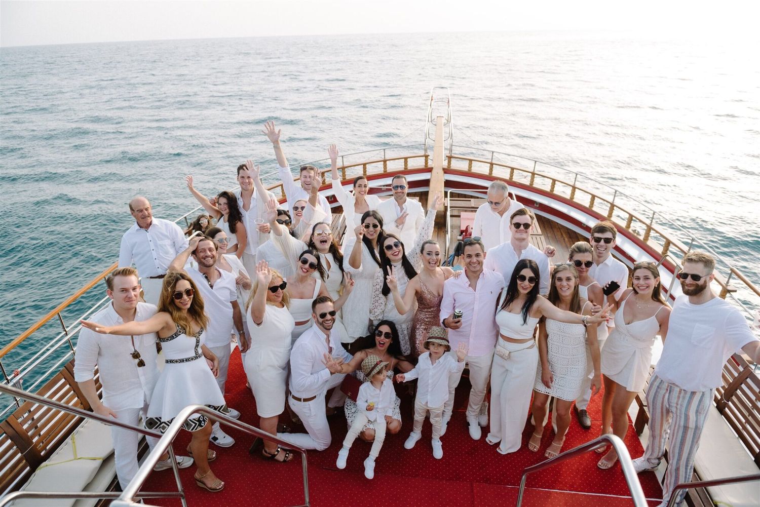 A group in white attire gathers on a yacht deck during a sunset cruise celebration at Parga