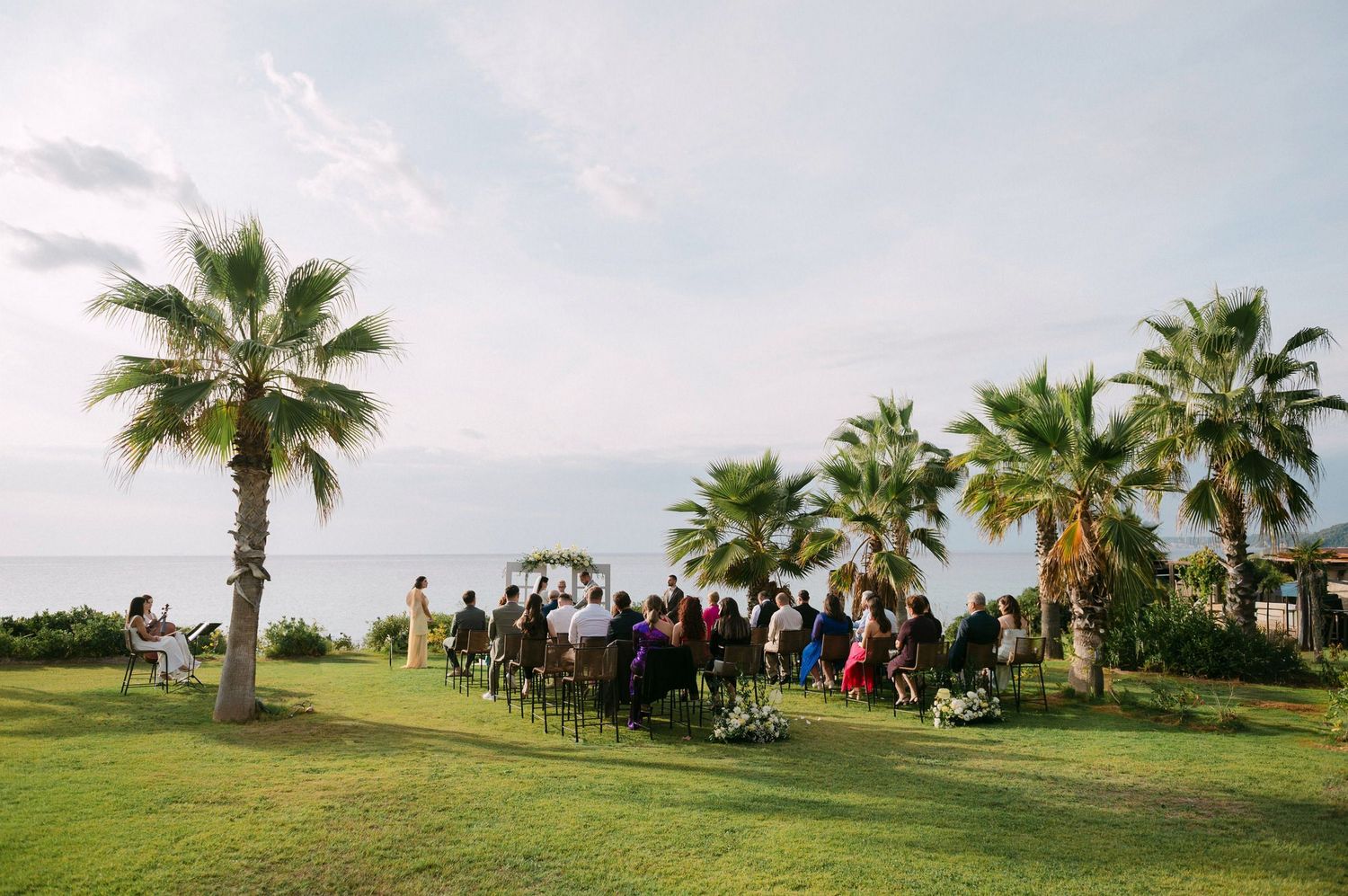 Outdoor wedding ceremony setup on a lush green lawn with palm trees and ocean views at a tropical destination venue.