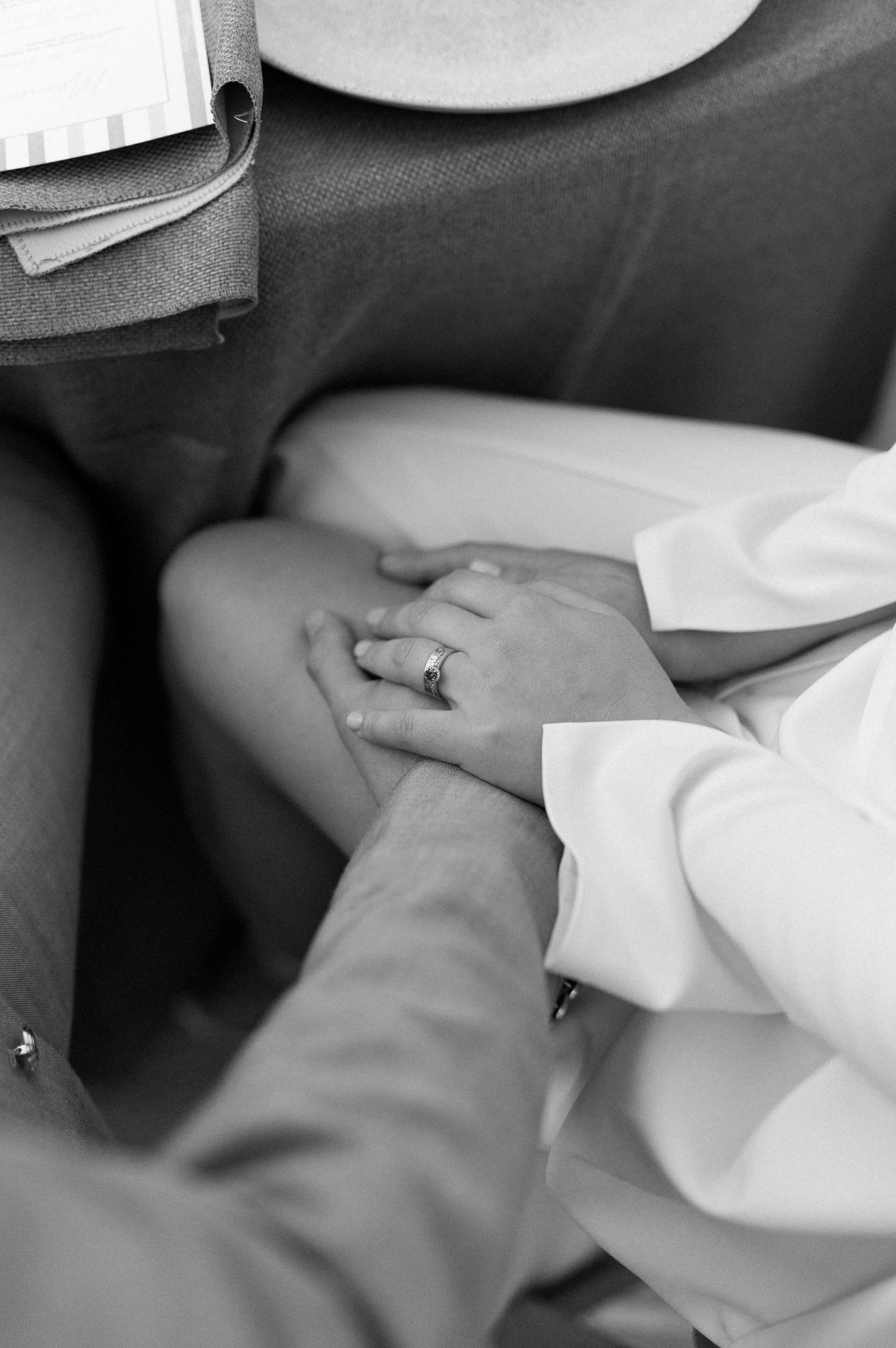 Black and white close-up of hands with wedding ring touching in an intimate romantic moment.