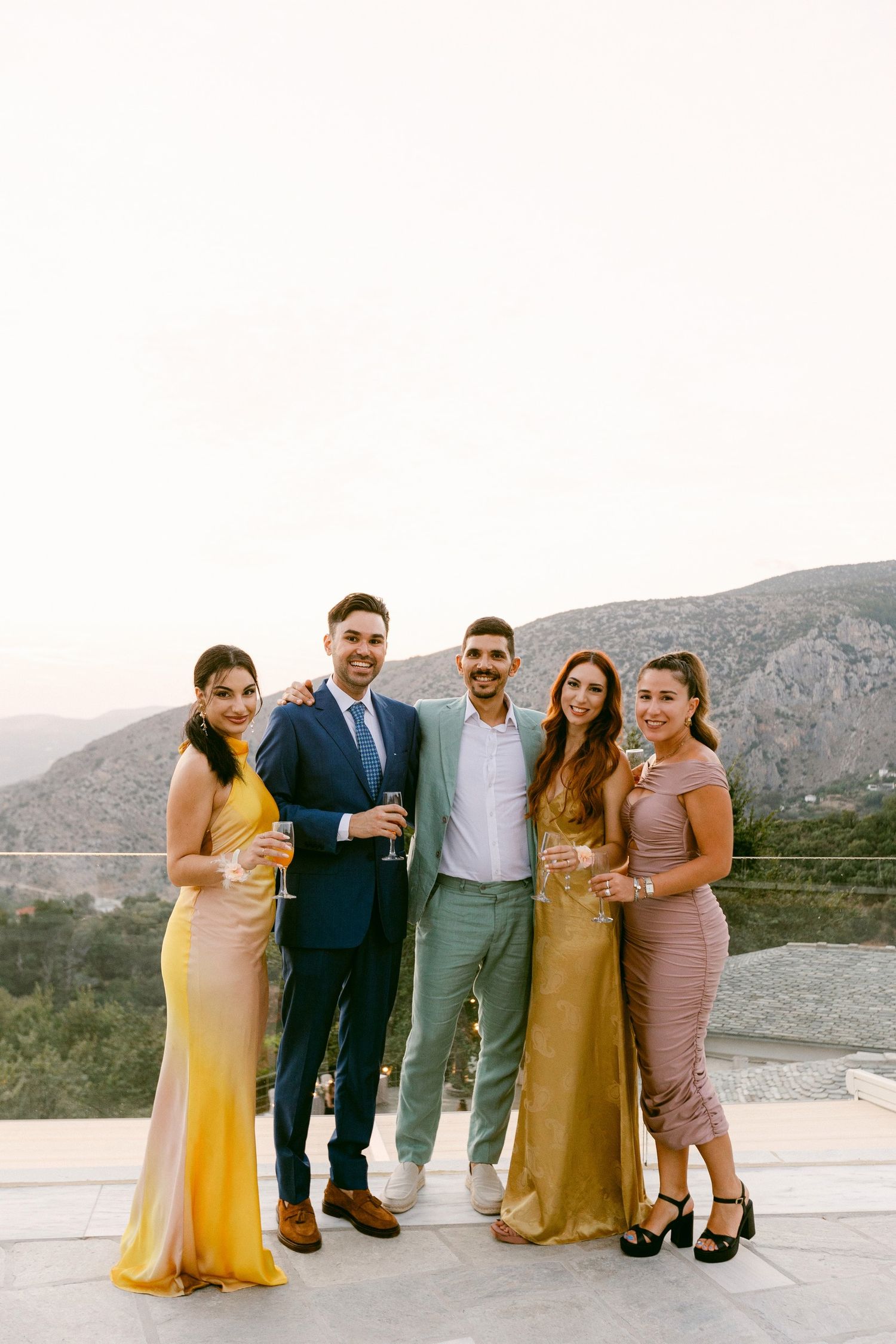 Group of friends dressed elegantly posing together on a terrace with mountains in the background at sunset.