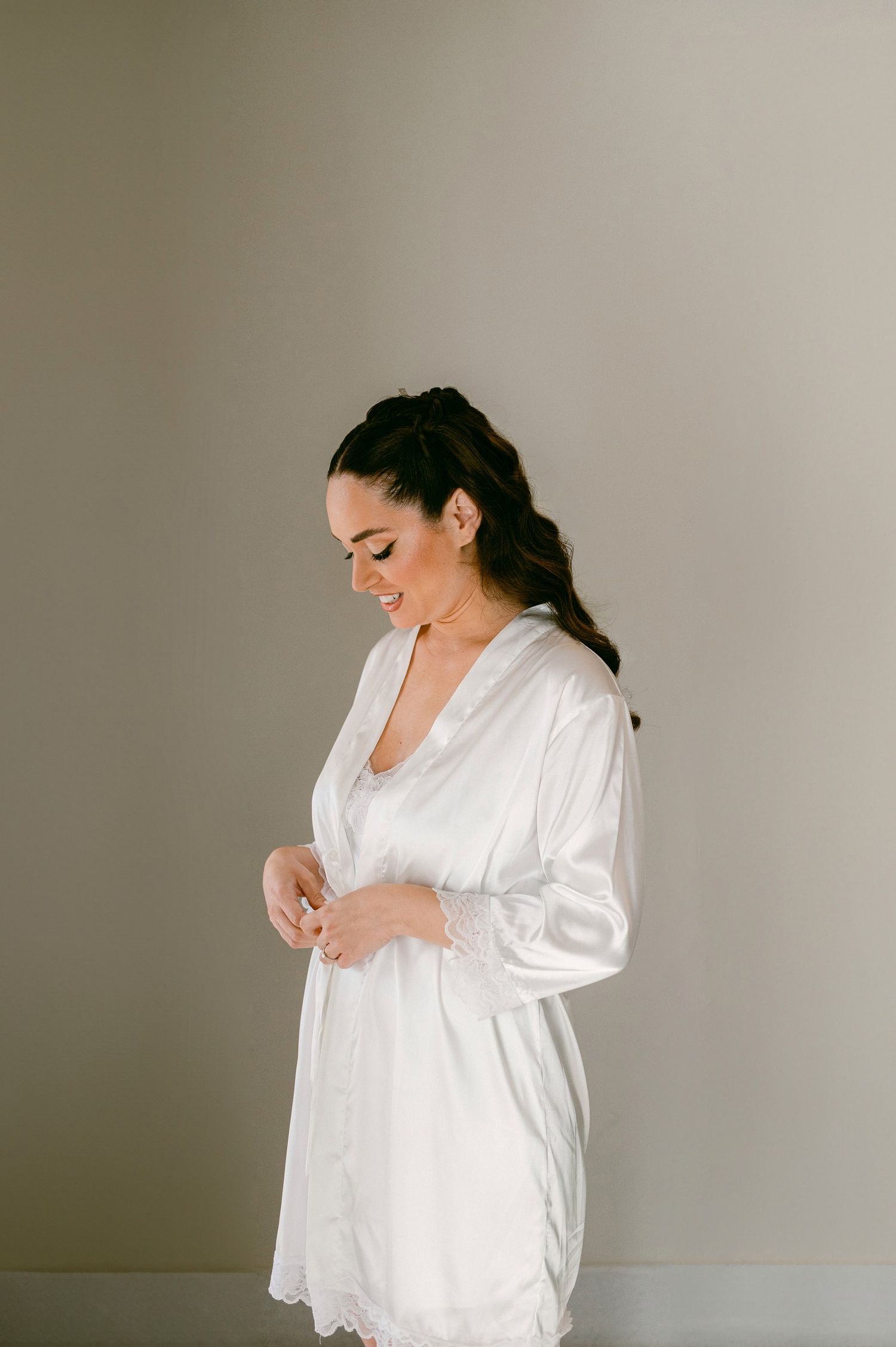 A person in a flowing white robe smiles while standing against a neutral wall.
