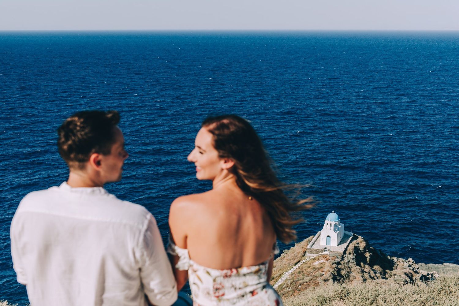Wind-swept couple enjoying panoramic ocean views from coastal cliff overlook.