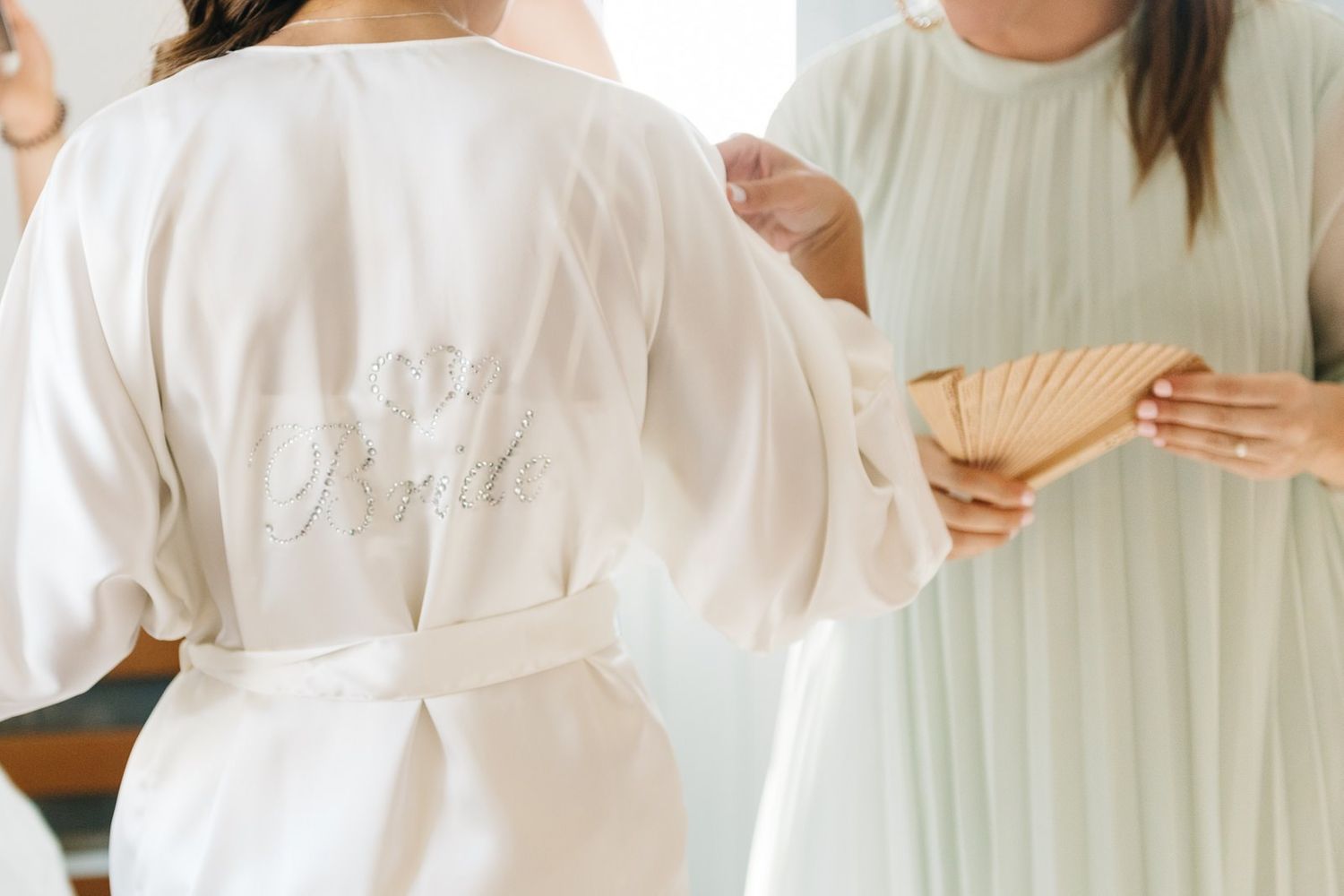 Close-up of white bridal robe with embroidery detail as someone holds a decorative fan.