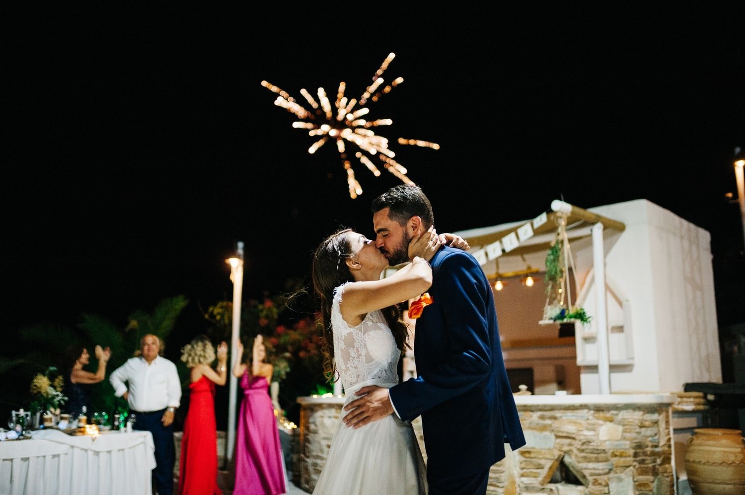 Wedding couple embracing under sparkling fireworks at outdoor reception.