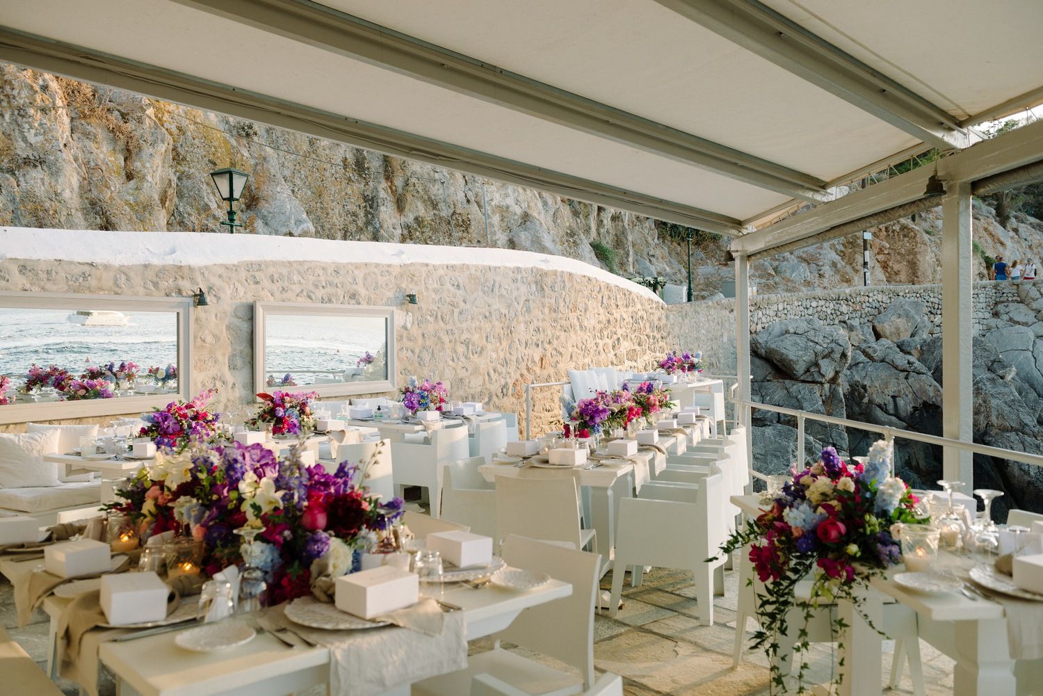 Elegant wedding reception setup with purple floral centerpieces in white coastal venue.