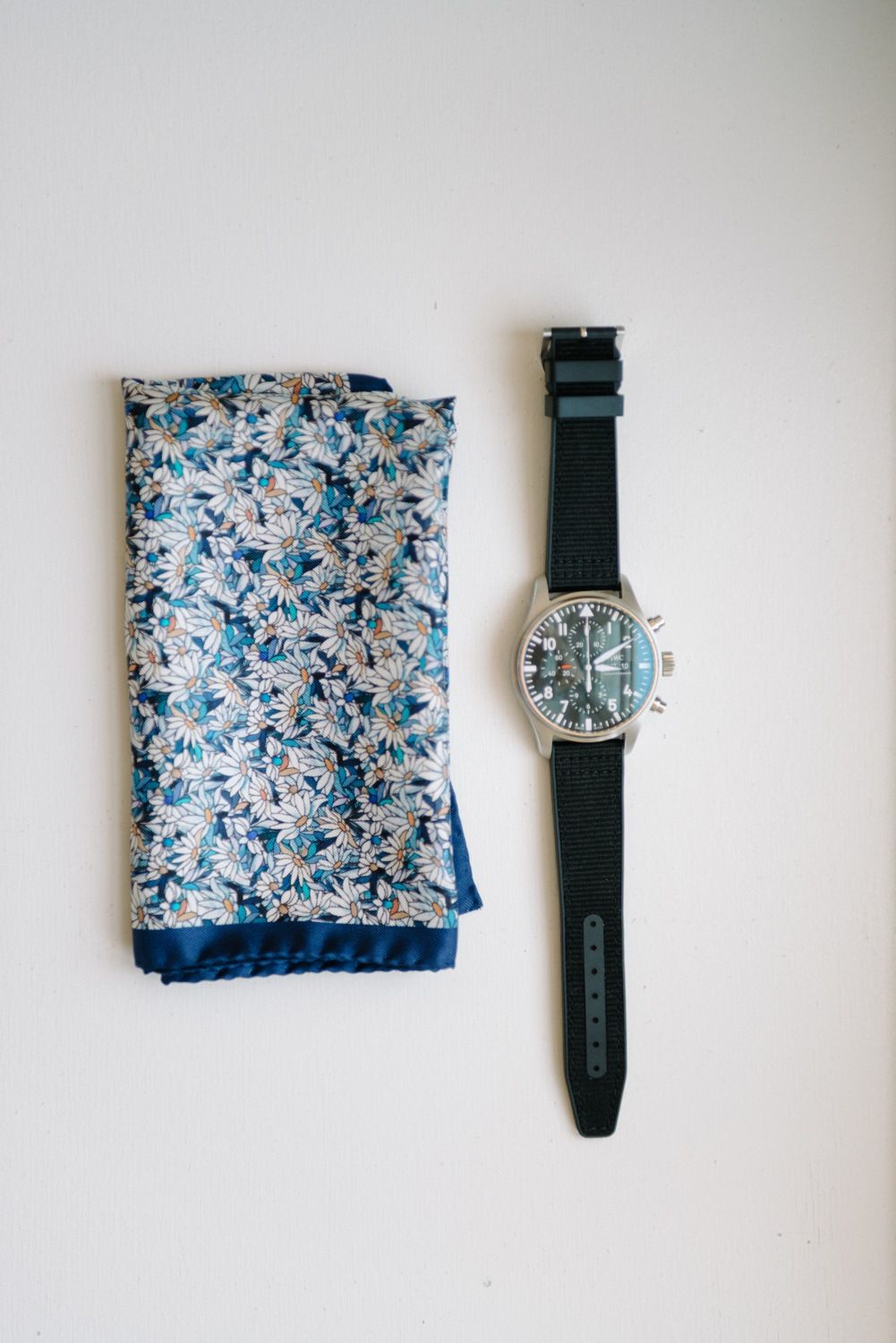 Blue floral pocket square and black watch displayed on white surface.