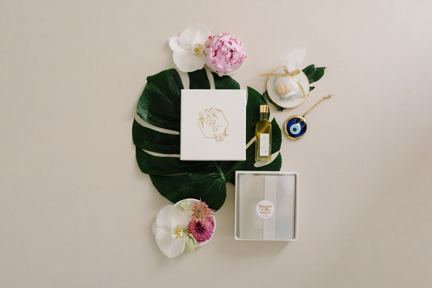 Wedding stationery flatlay with white roses, pink peonies, and a green monstera leaf on neutral background.