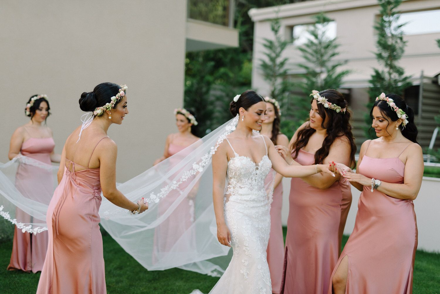 Joyful outdoor wedding scene with bridesmaids in pink dresses arranging the bride's veil.