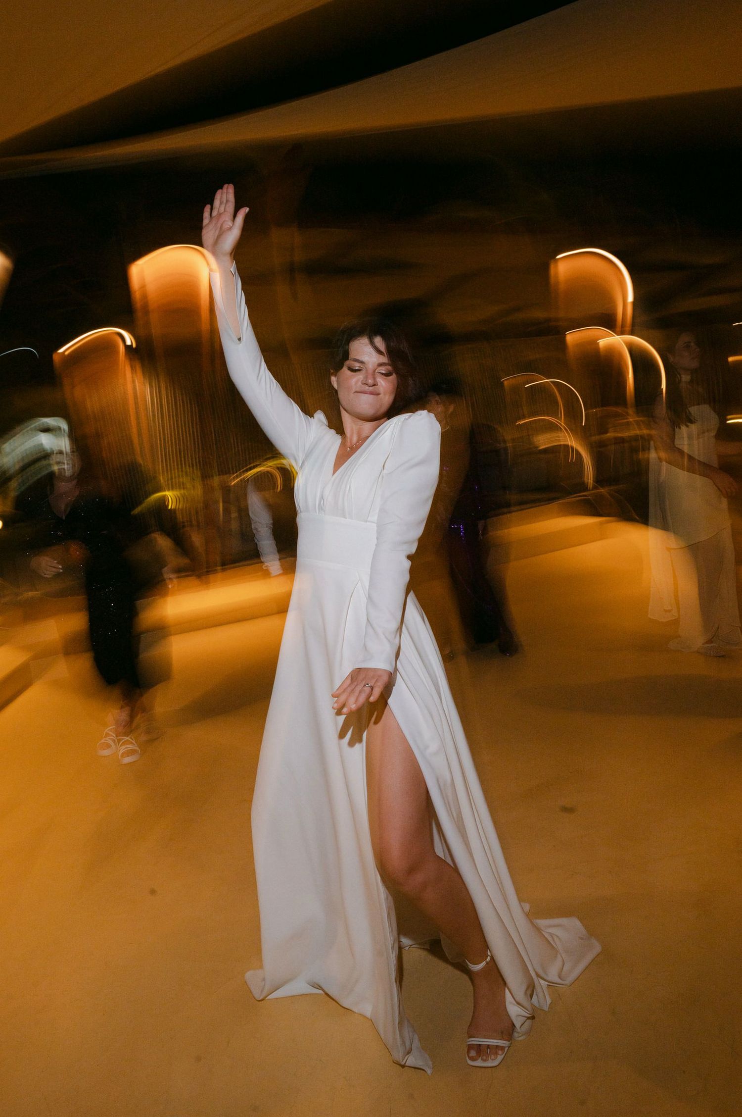 A figure in white flowing garments dances and twirls in a dimly lit space creating a dreamy motion blur effect.