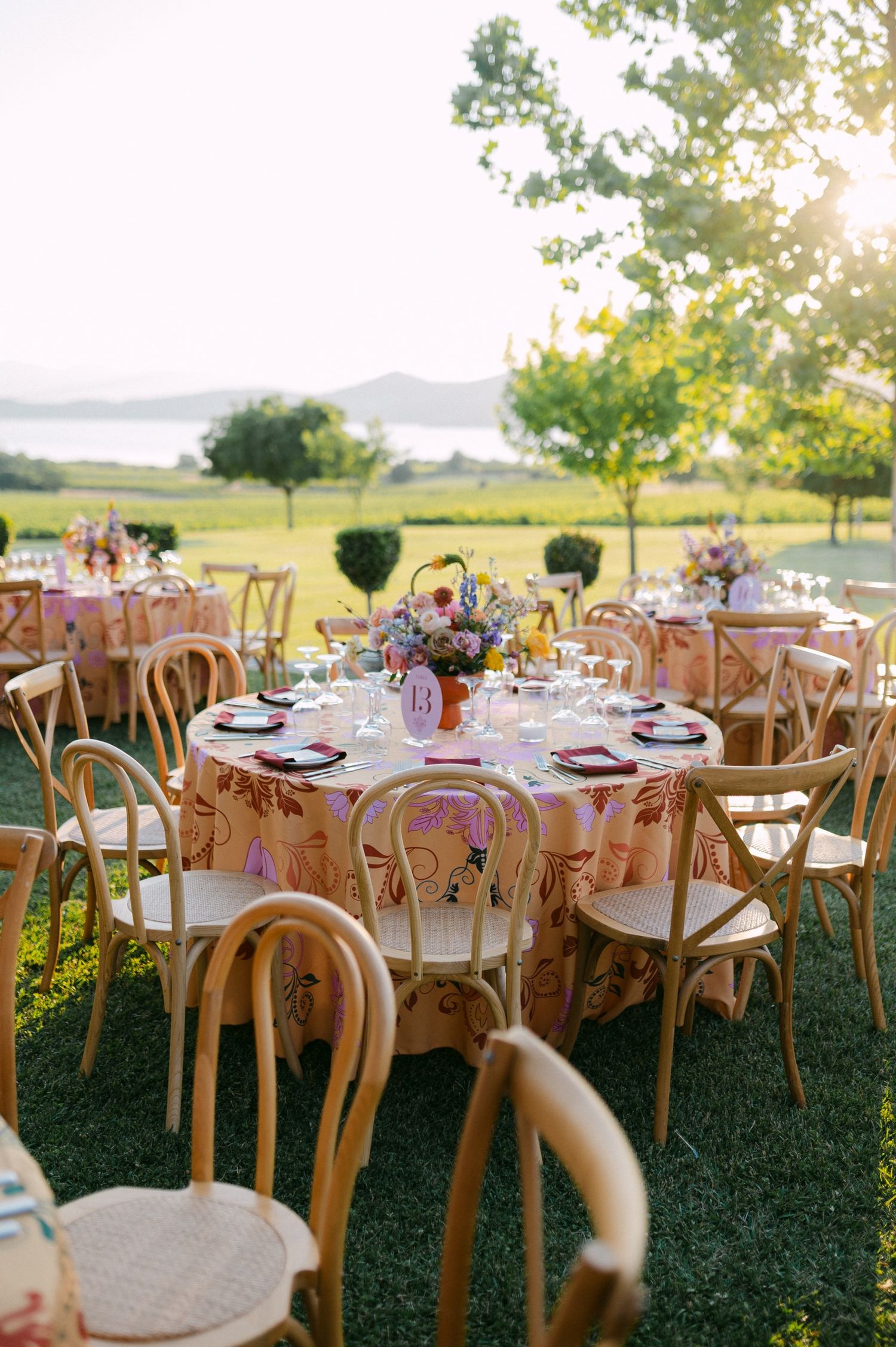 Elegant outdoor wedding reception setup with wooden chairs and round tables decorated with peach tablecloths.