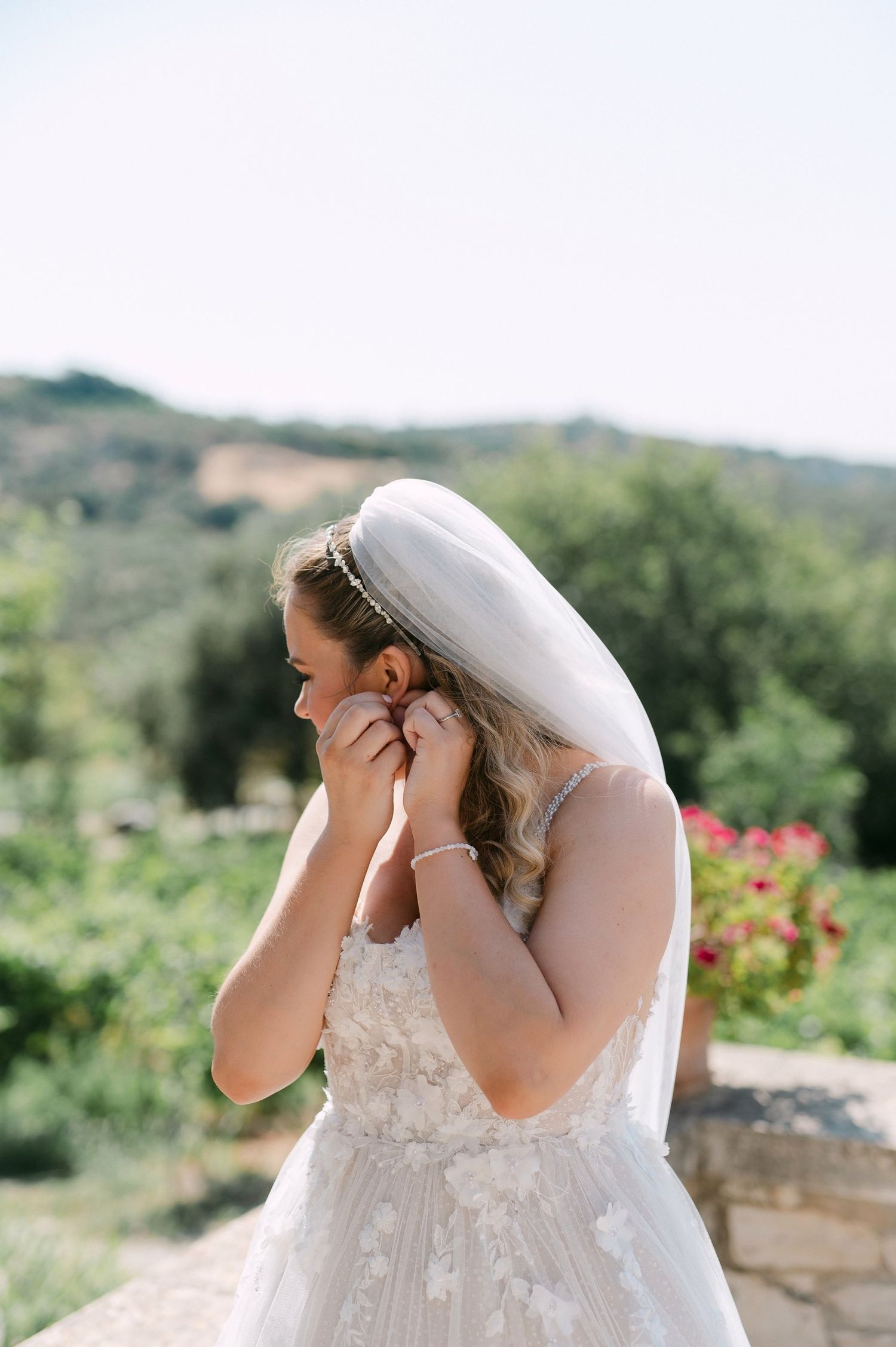 Bride in a white lace wedding dress leans back in a dramatic pose against a scenic outdoor background.