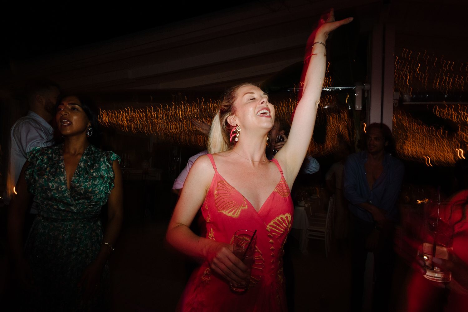 Guest in red dress dances joyfully under ambient reception lighting.