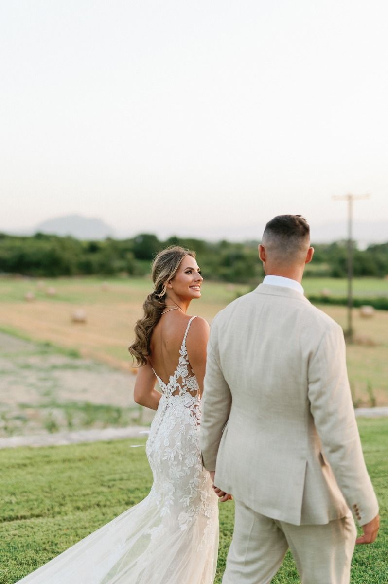 Elegant couple in wedding attire walking across manicured lawn with mountain views.