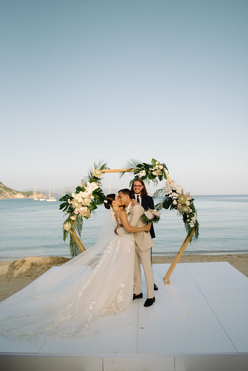 Couple embraces under an elegant flower arch at their seaside destination wedding.