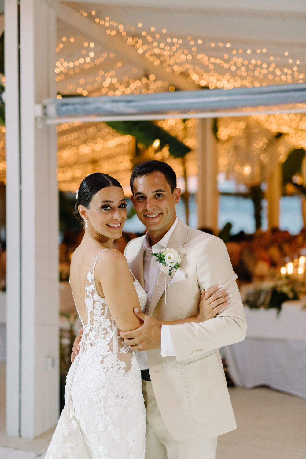Newlyweds pose together in formal attire under warm glowing reception lights.